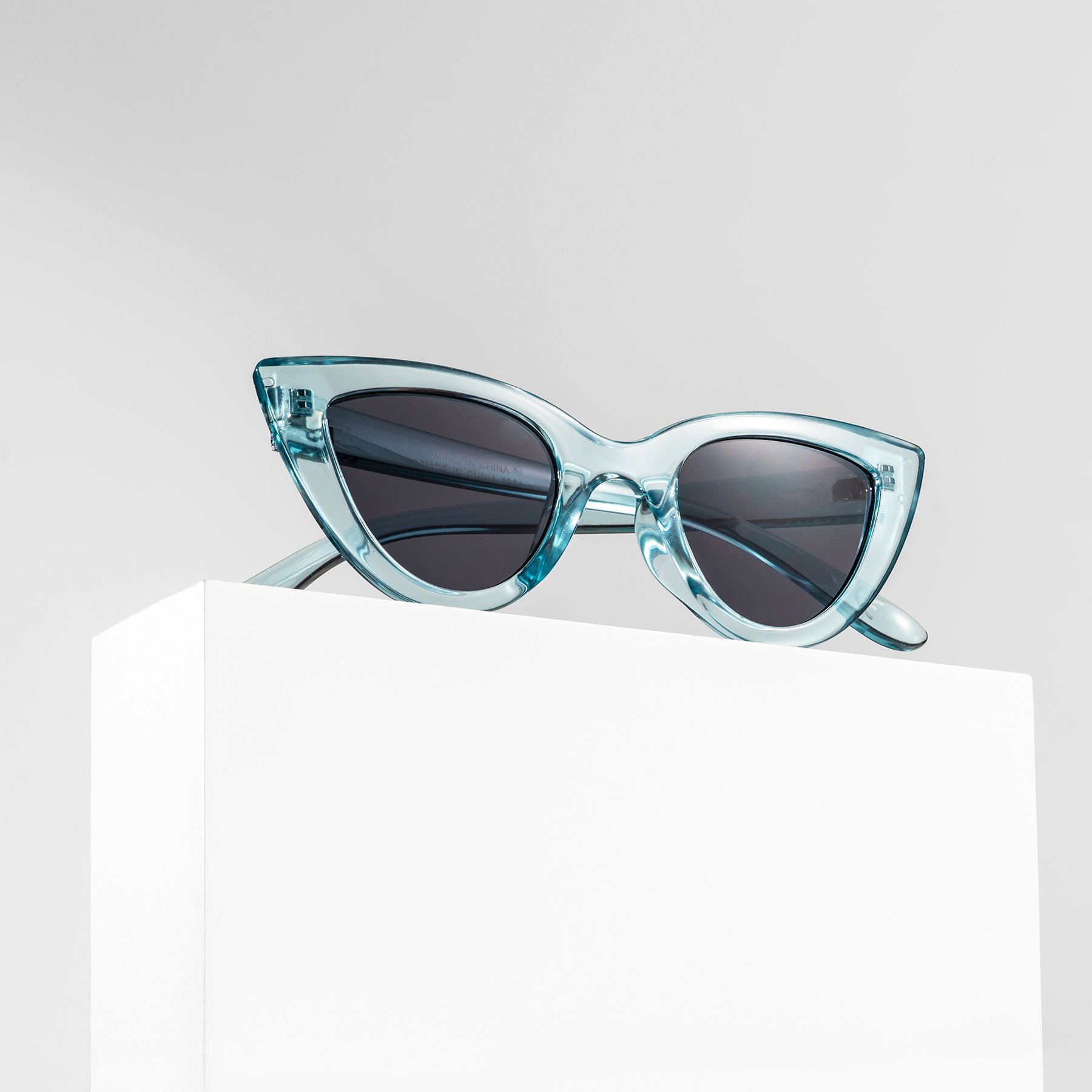 One rectangular white product photography riser displaying a pair of blue sunglasses