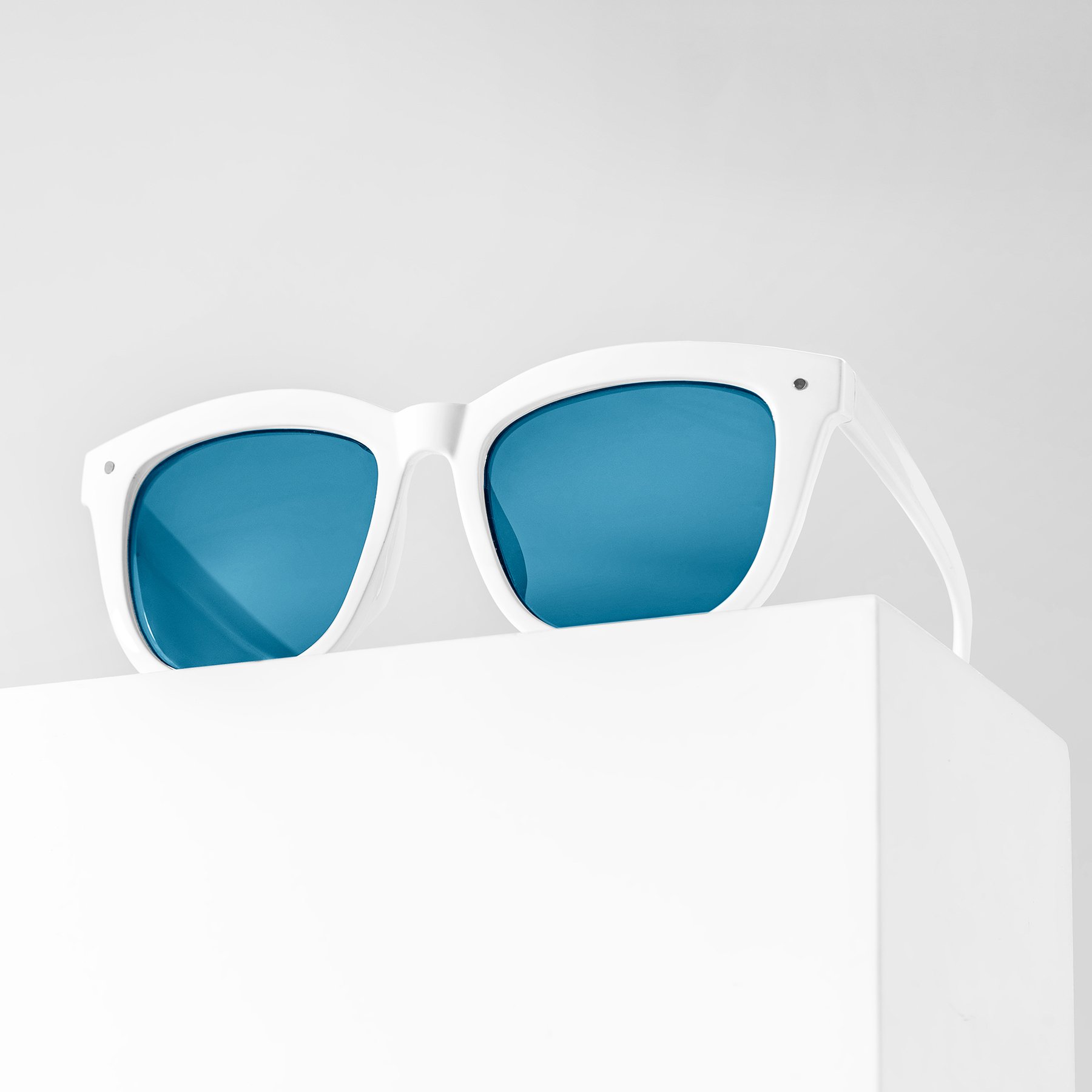 White product photography riser displaying white sunglasses with blue lenses