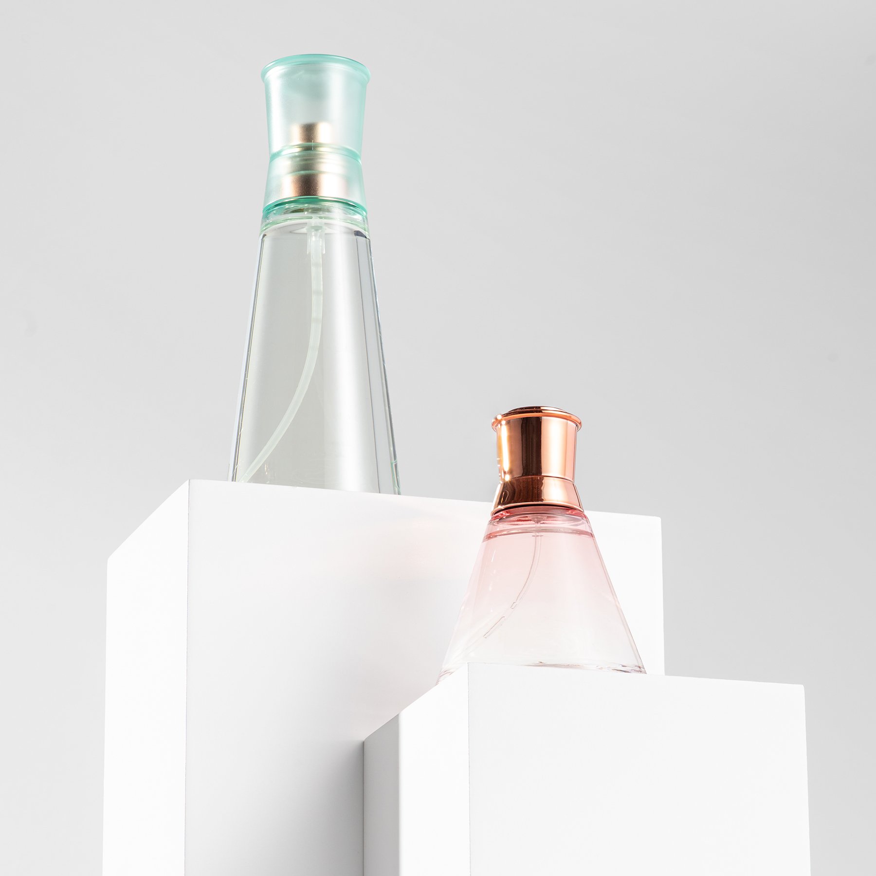 Two white product photography boxes displaying pink and green perfume bottles
