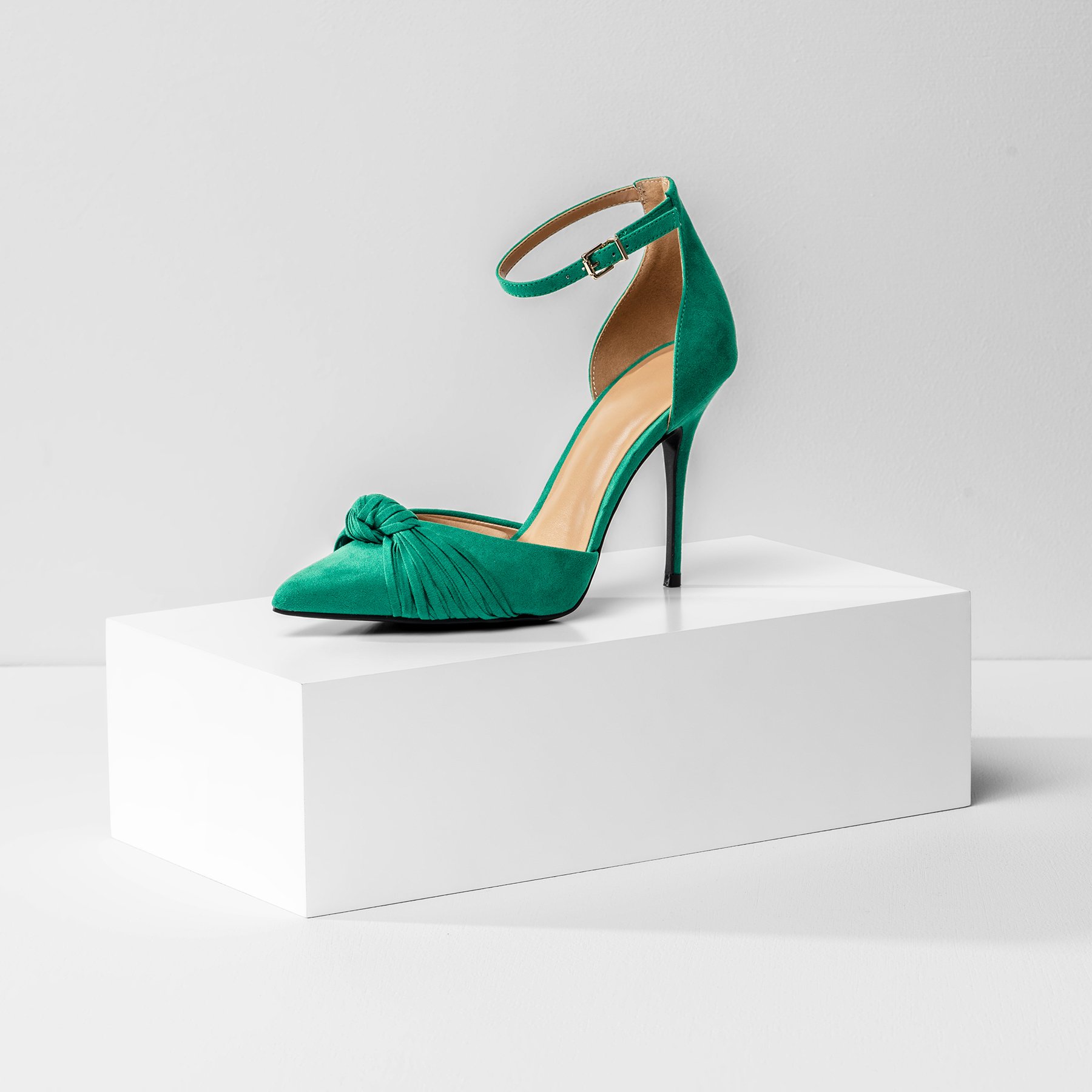 One white product photography riser the size of a shoebox, displaying a green high heel shoe on a white background