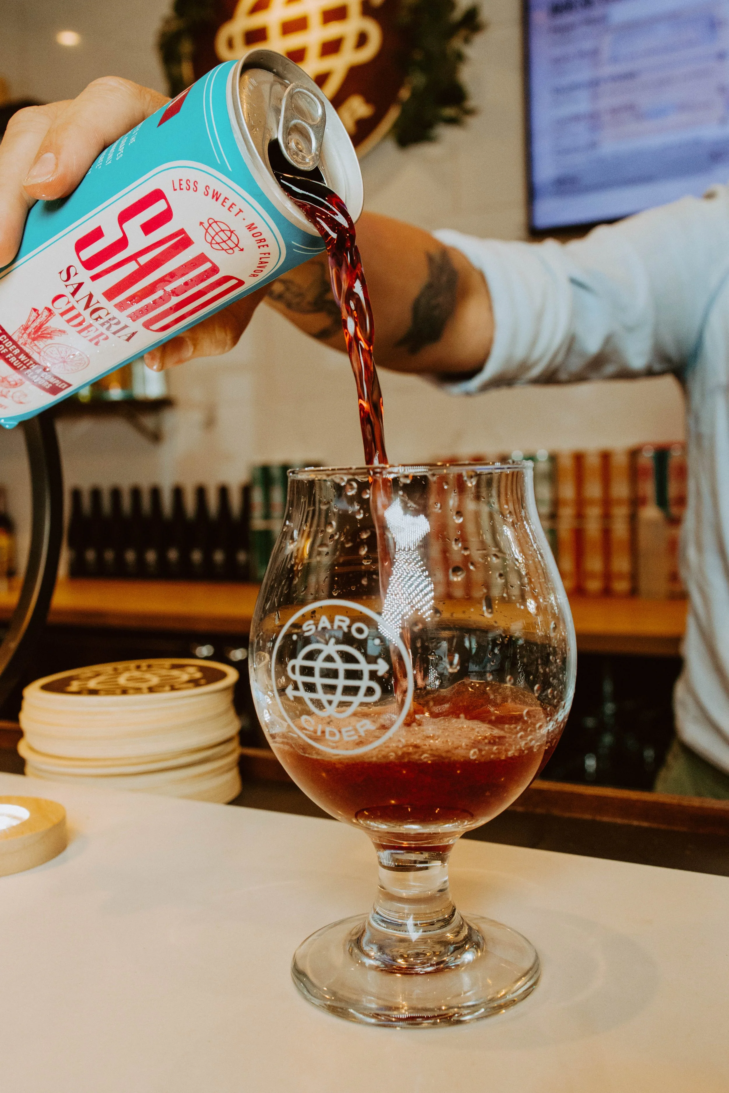 Pouring Saro cider into a glass at a bar with a cocktail in progress.