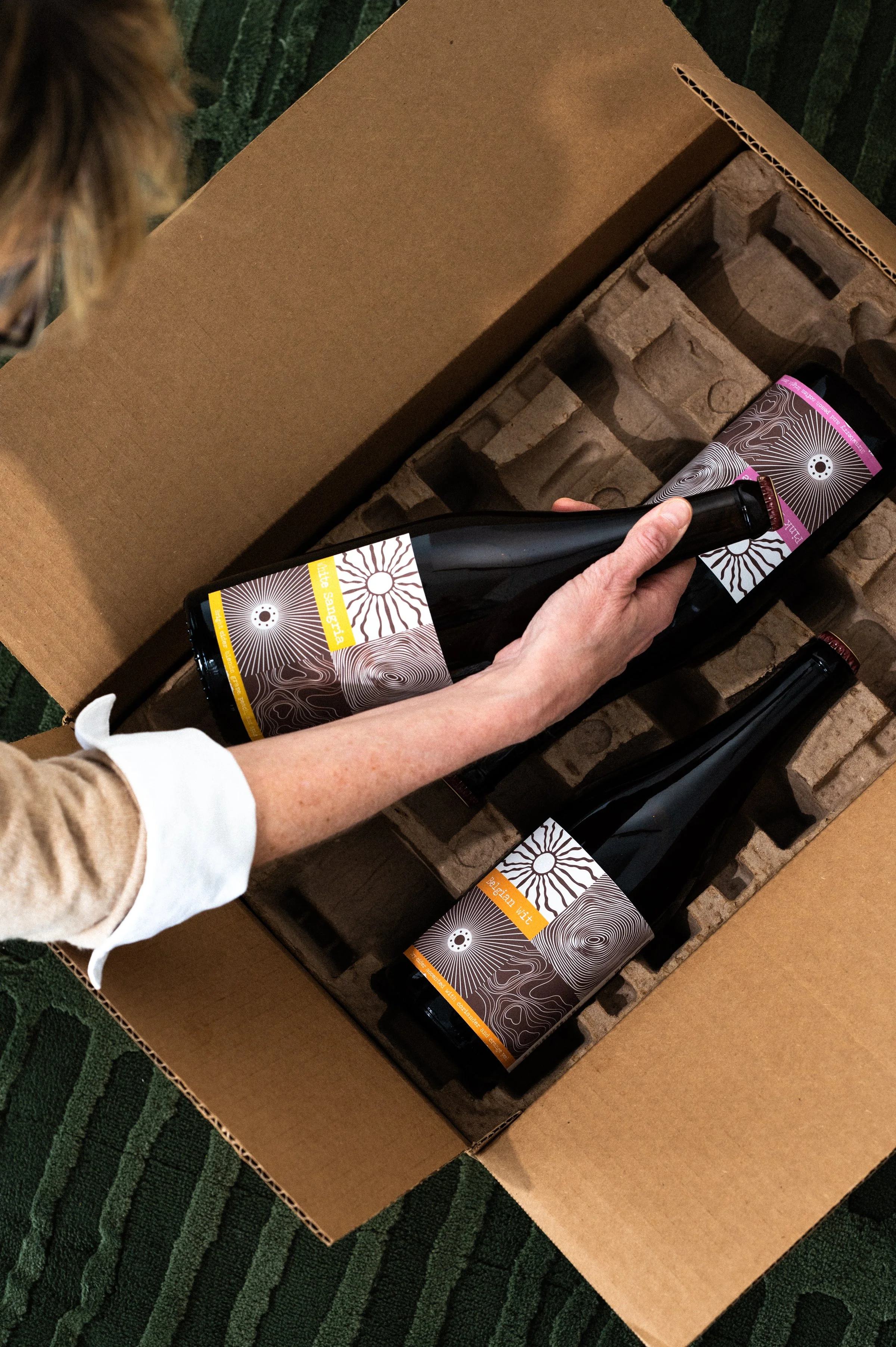 Hand holding a Saro whiskey barrel aged sour cherry beverage bottle in front of a large wooden barrel labeled "World Cooperage".