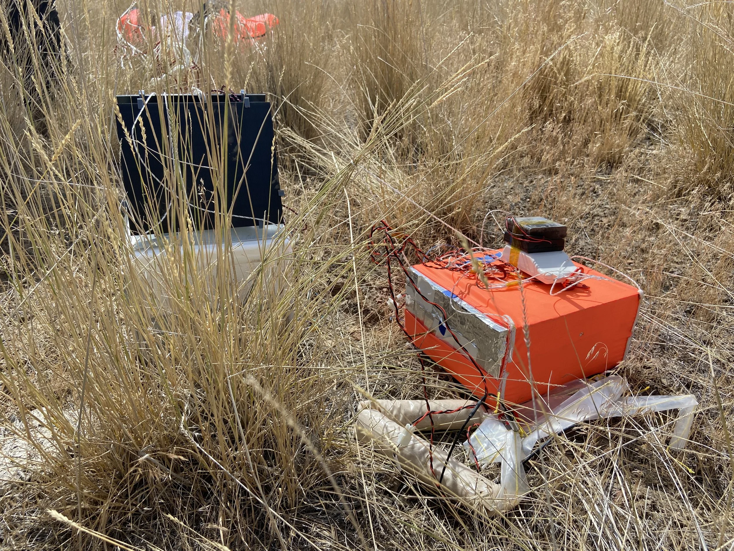 A scientific device, possibly a weather or environmental sensor, situated in a dry, grassy field with tall, yellowish grass.