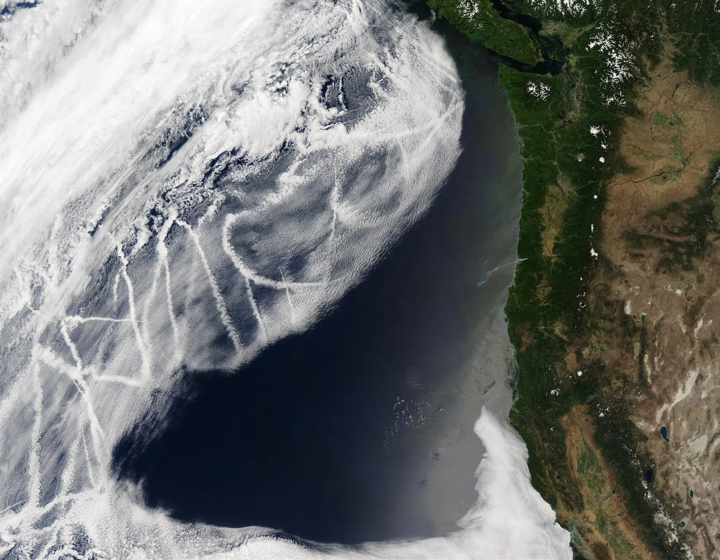 Satellite image of a large storm over the Pacific Northwest coast, with cloud formations and contrails from aircraft visible.