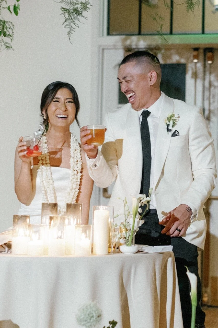 A couple smiling and laughing during their wedding toasts while holding cocktails
