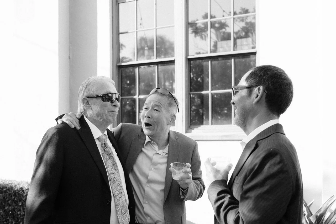 Three older men catching up over drinks at a wedding during cocktail hour. Black and white wedding photography