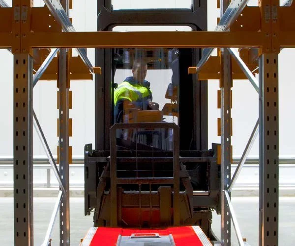 Warehouse operator in high-visibility gear operating forklift between automated racking systems with integrated shuttle technology