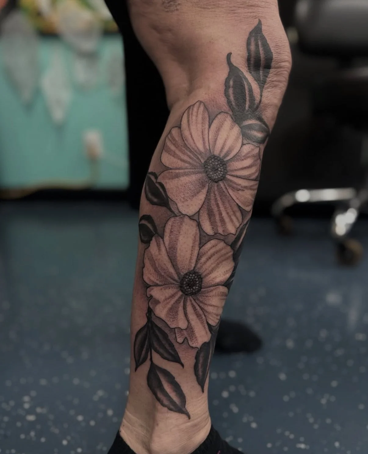 Black and gray floral tattoo on a person's forearm featuring large flowers and leaves.