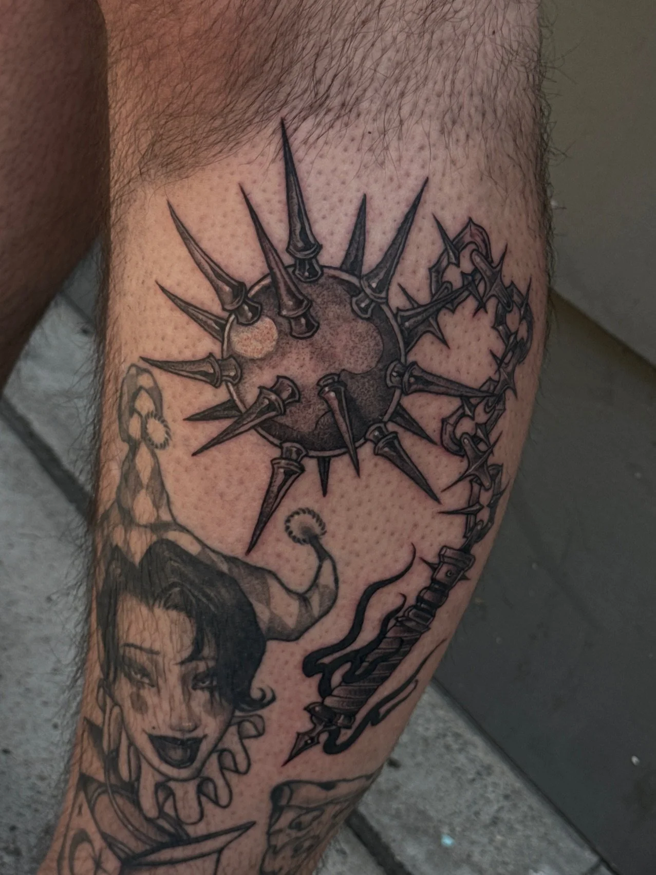 Black and gray tattoo of a woman with dark hair and lipstick, eyes closed, smiling, with a star-shaped element around her neck, and a large flail. The tattoo is on a person's upper thigh.