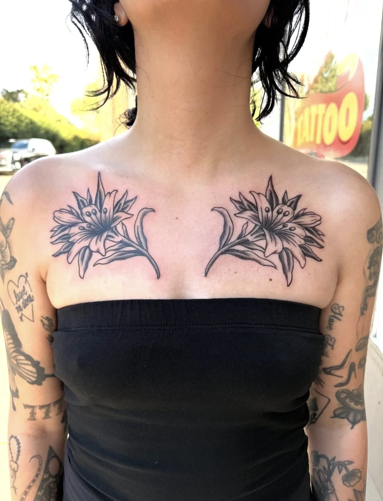 Tattooed woman with floral tattoos on her chest, wearing a black strapless top, outside a tattoo shop in carson city nevada
