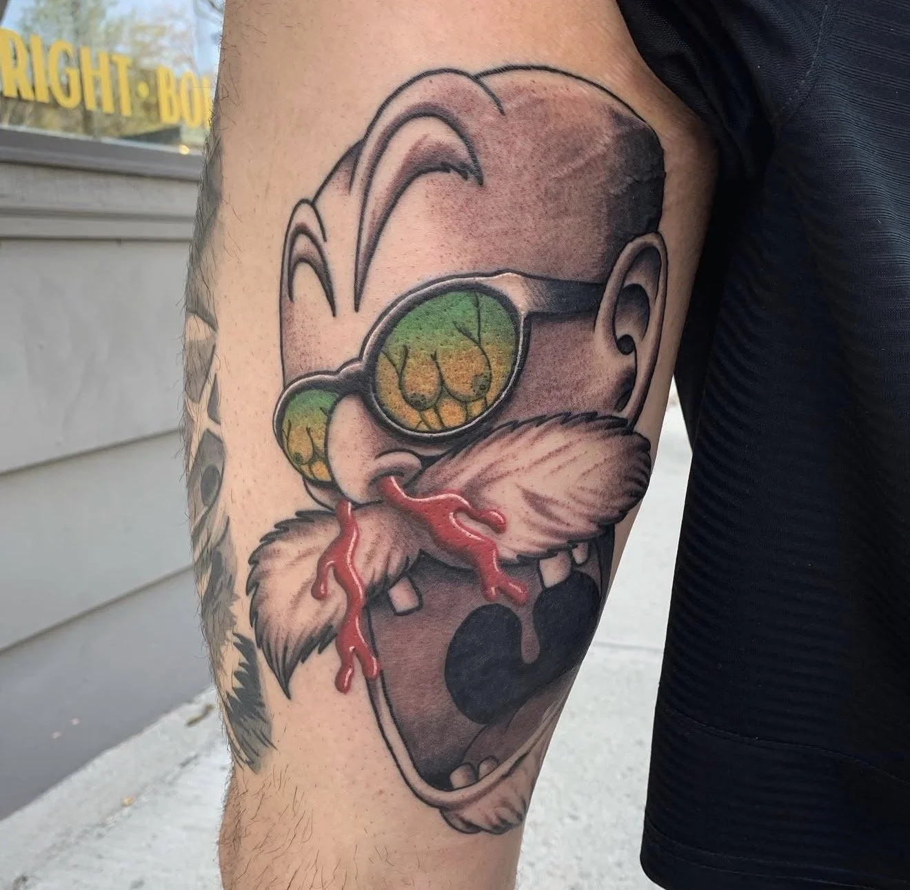 Tattoo of cartoon dog character with sunglasses, open mouth, and red tongue.