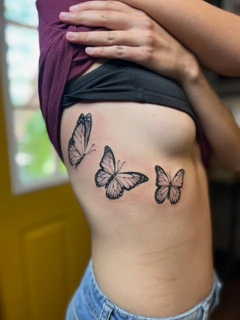A person lifting their shirt to reveal a butterfly tattoo on their side.