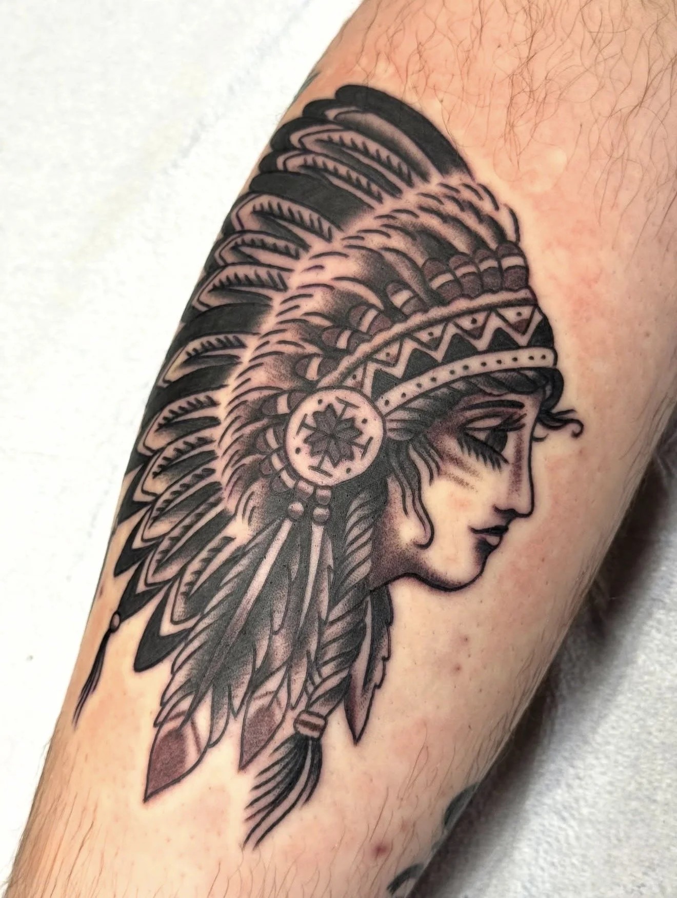 Black and grey traditional tattoo of a Native American woman's profile wearing a feathered headdress.