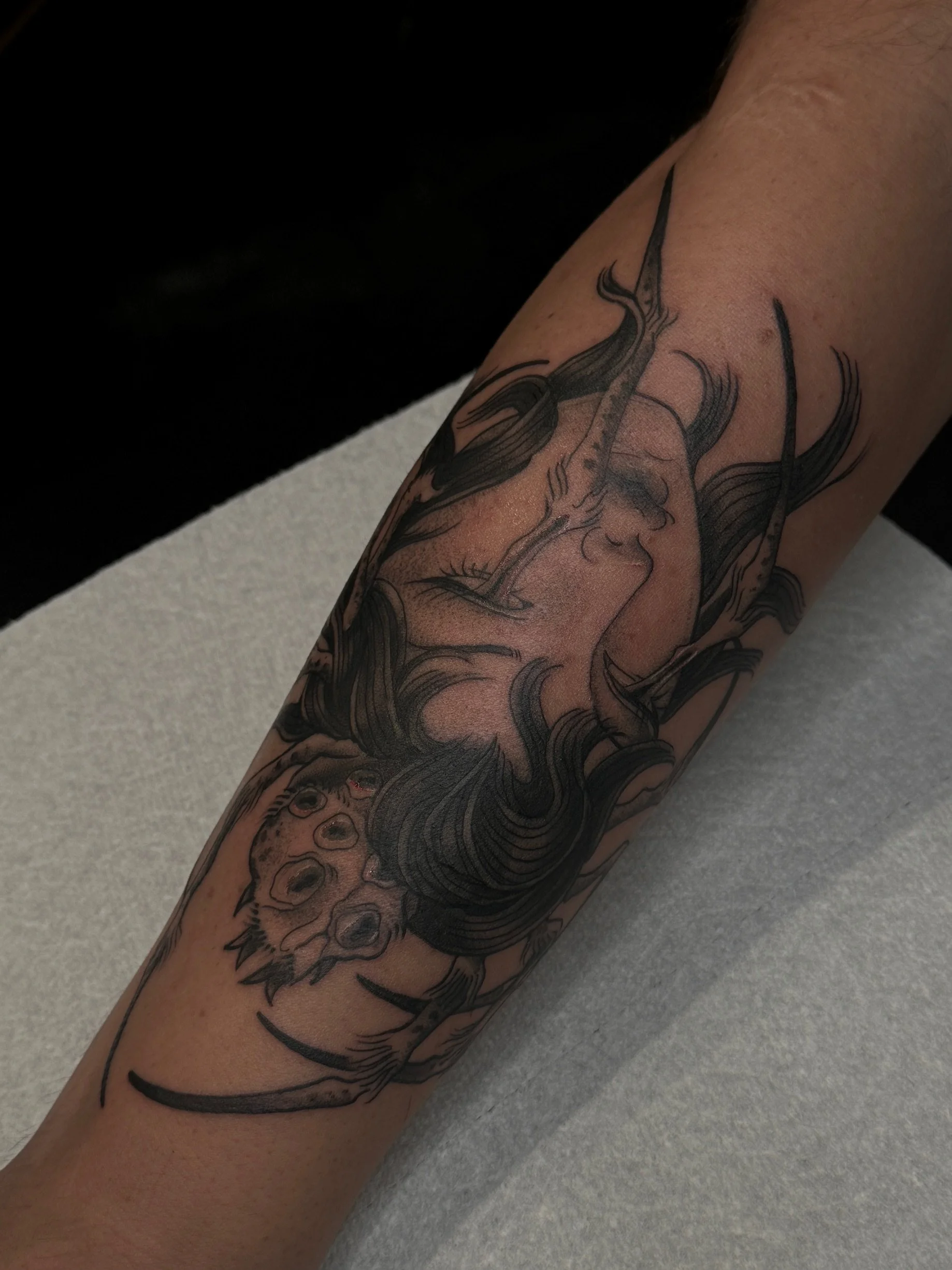 Black ink tattoo of a woman's face with flowing hair and a wolf's head with bared teeth, covering the lower arm.