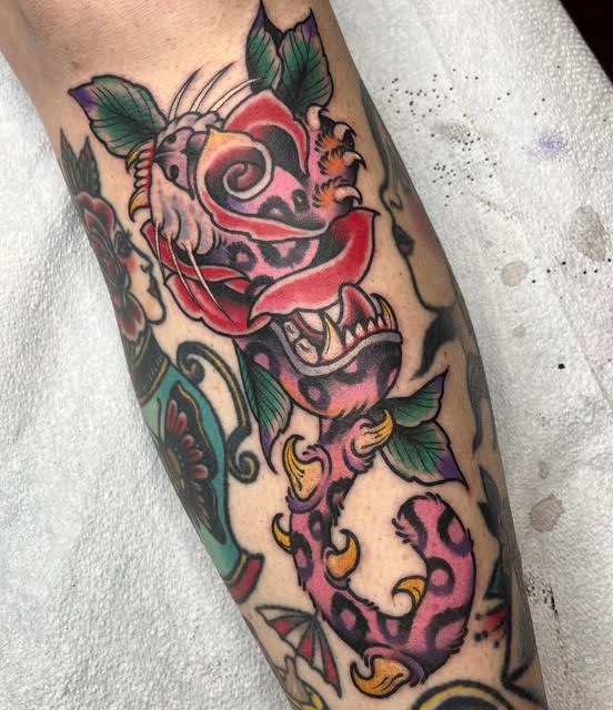 Tattoo of a colorful, stylized creature with a skull and floral elements, featuring bold lines and vibrant colors.