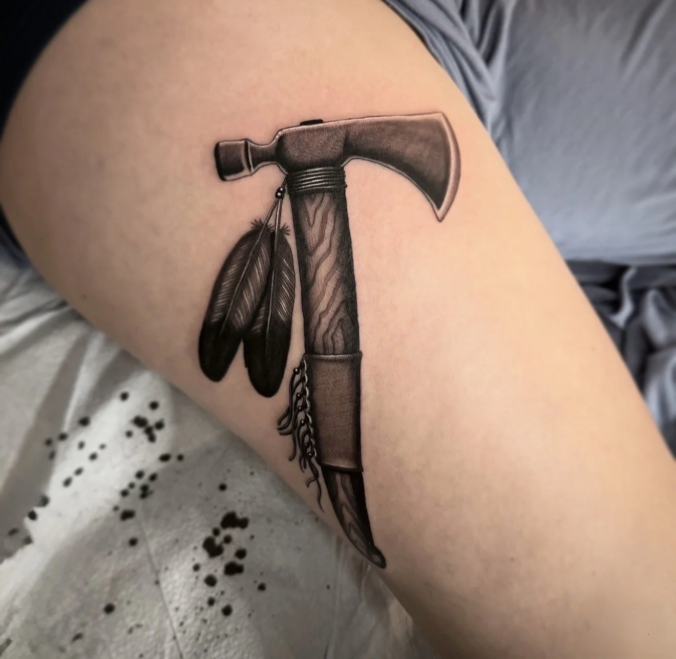 Tattoo of a hammer with feathers hanging from it, inked on a person's upper arm.