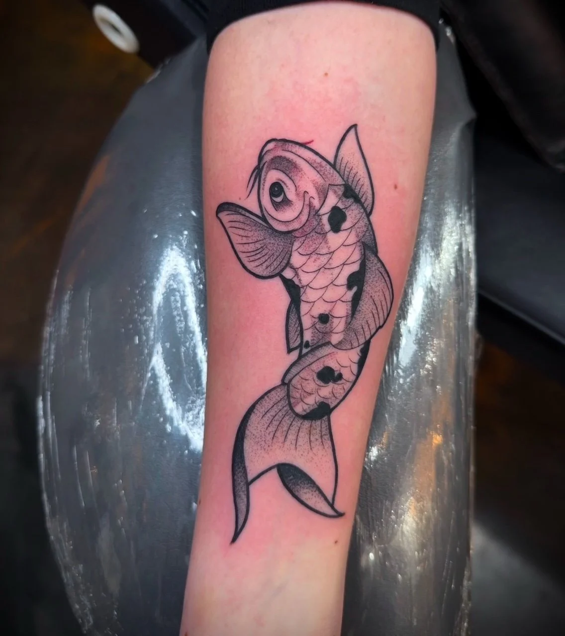 Black outline tattoo of a koi fish on a person's forearm.