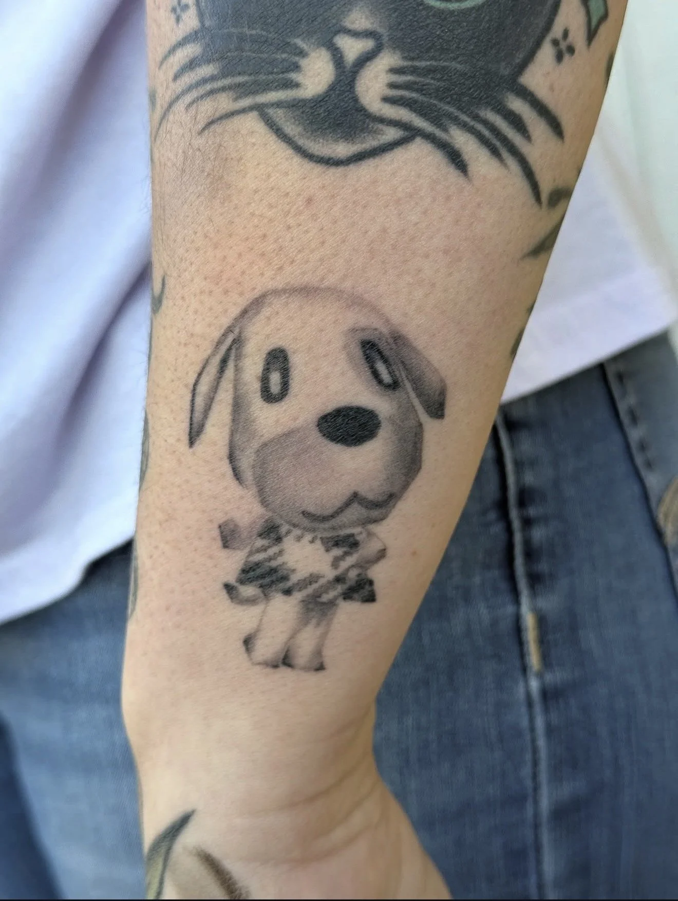 Tattoo of a cute, stylized dog with floppy ears and a friendly expression on a person's arm.