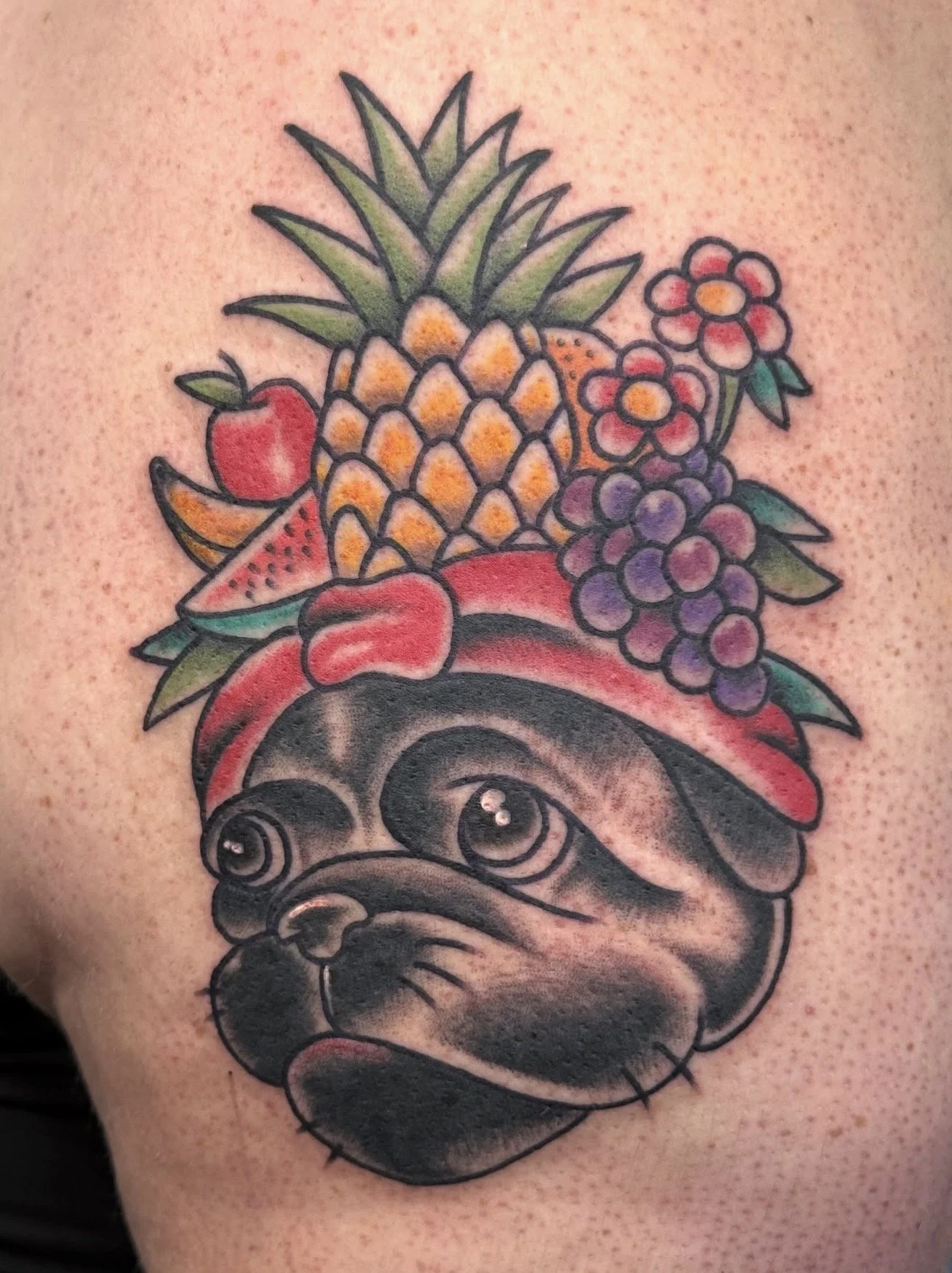 trad Tattoo of a French Bulldog wearing a red bandana with a pineapple, watermelon, strawberry, cherry, grapes, and flowers on its head.