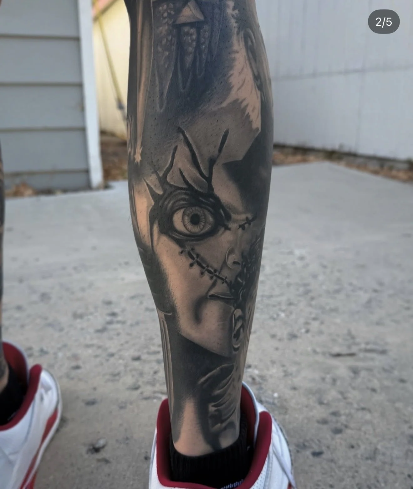 Tattoo of a stylized chucky face with detailed eye and stitched mouth on person's lower leg.