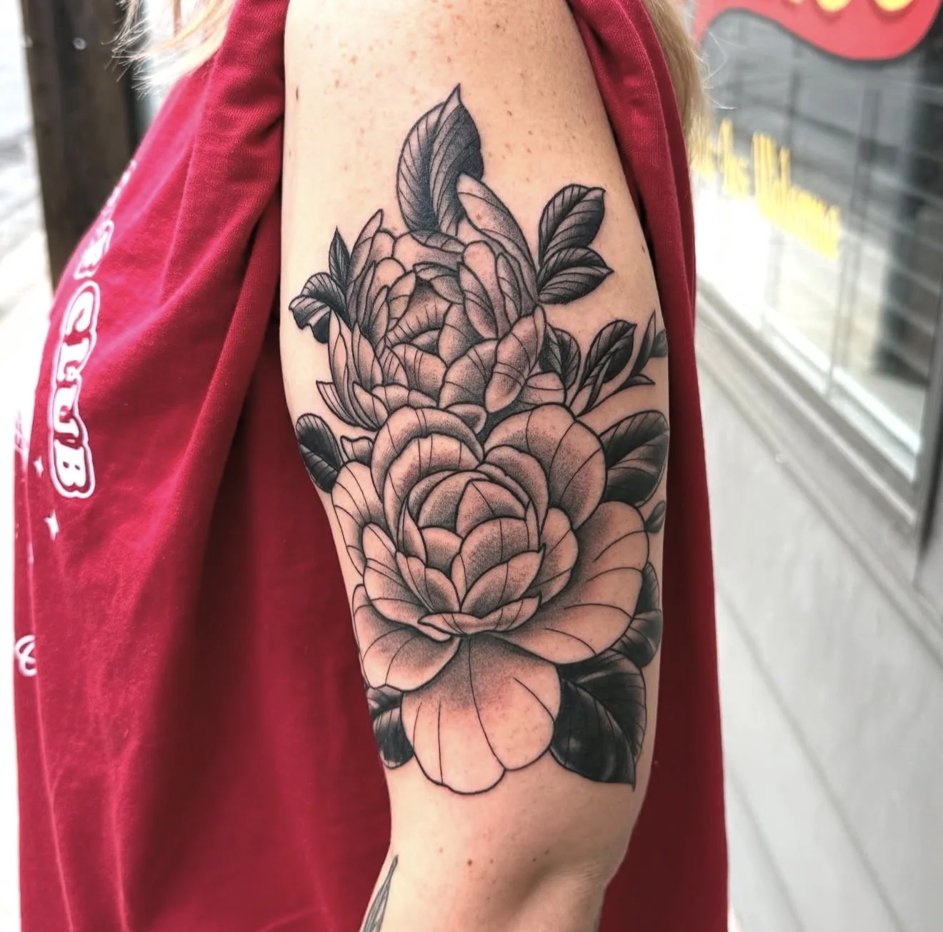 Black and gray floral tattoo on upper arm featuring large peony flowers and leaves.