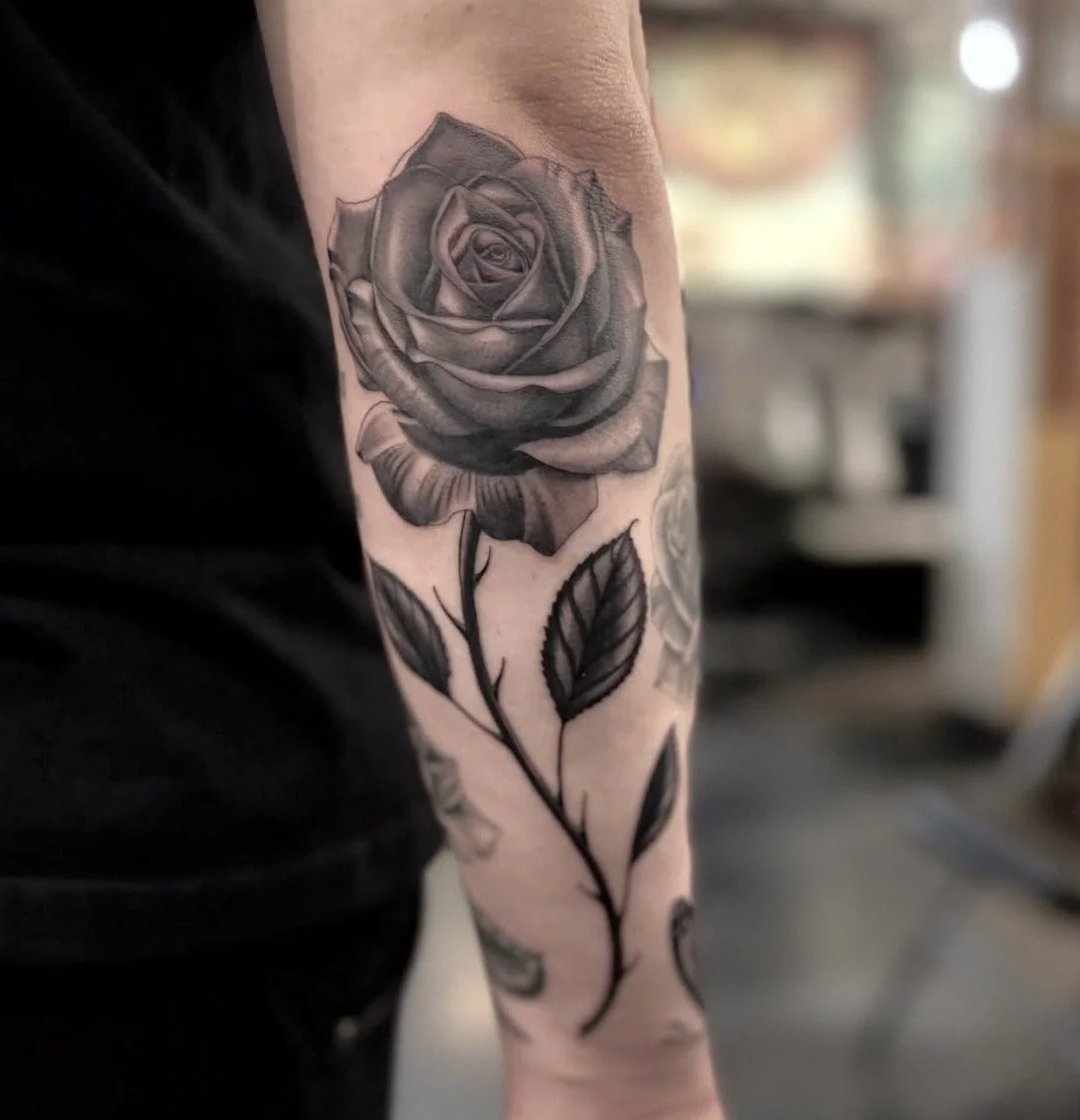 Black and gray realistic rose tattoo on person's arm with detailed petals and leaves.