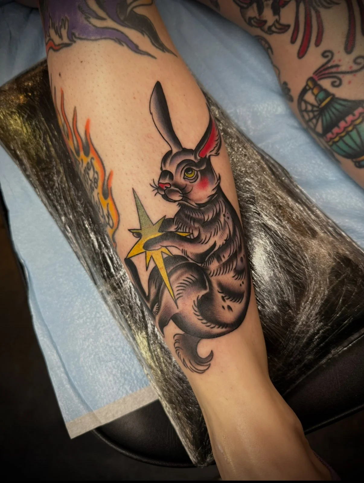 Tattoo of a rabbit holding a yellow star surrounded by flames on a person's arm.