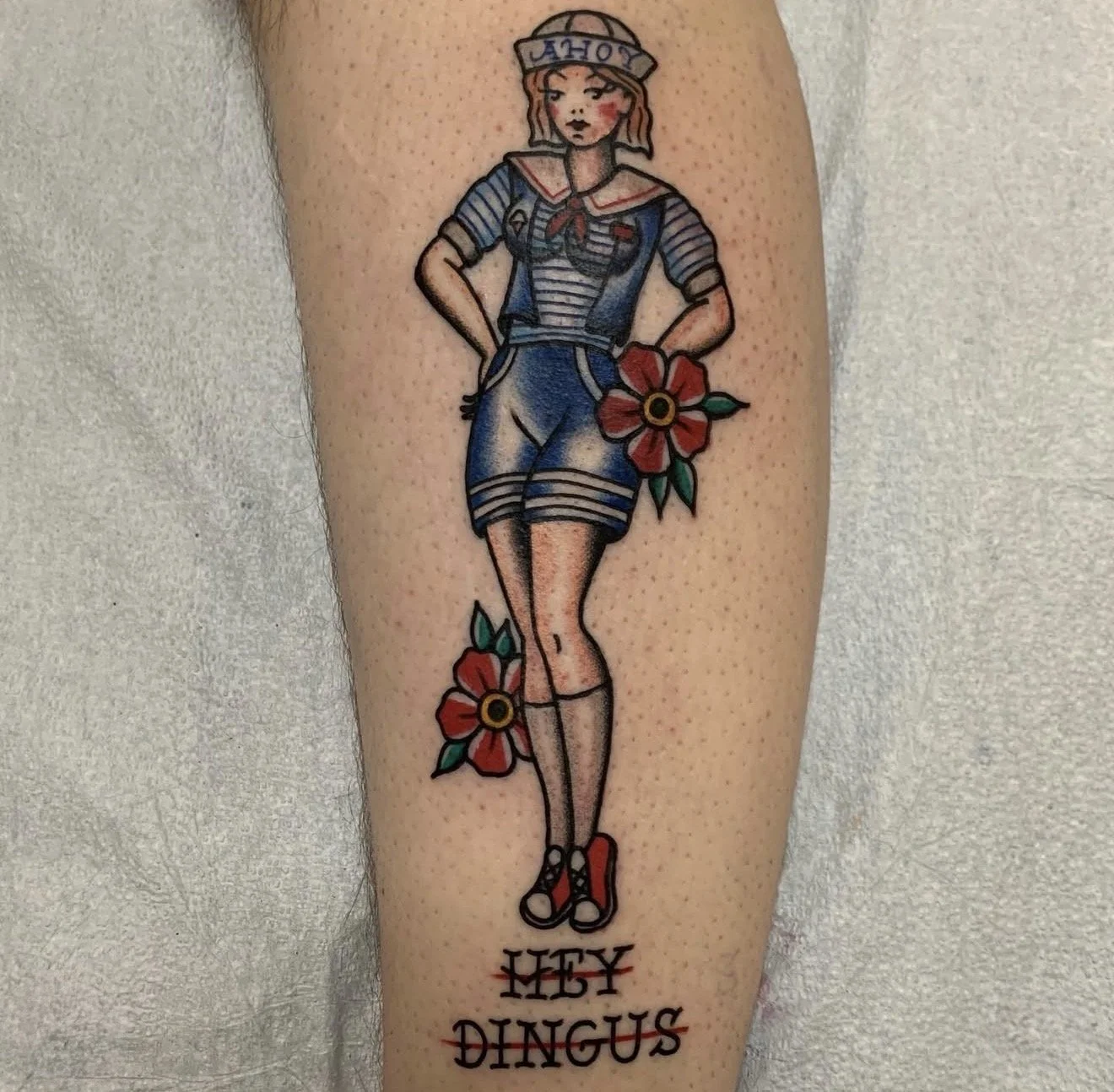 Colorful tattoo of a woman dressed in a sailor outfit with the word 'ahoy' on her hat, holding a large red flower, with the words 'HEY DINGUS' written below.