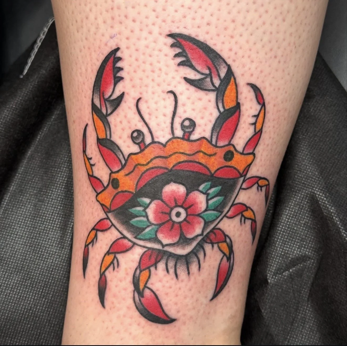 Colorful tattoo of a crab with a floral pattern on its body, featuring red, orange, black, green, and pink colors.