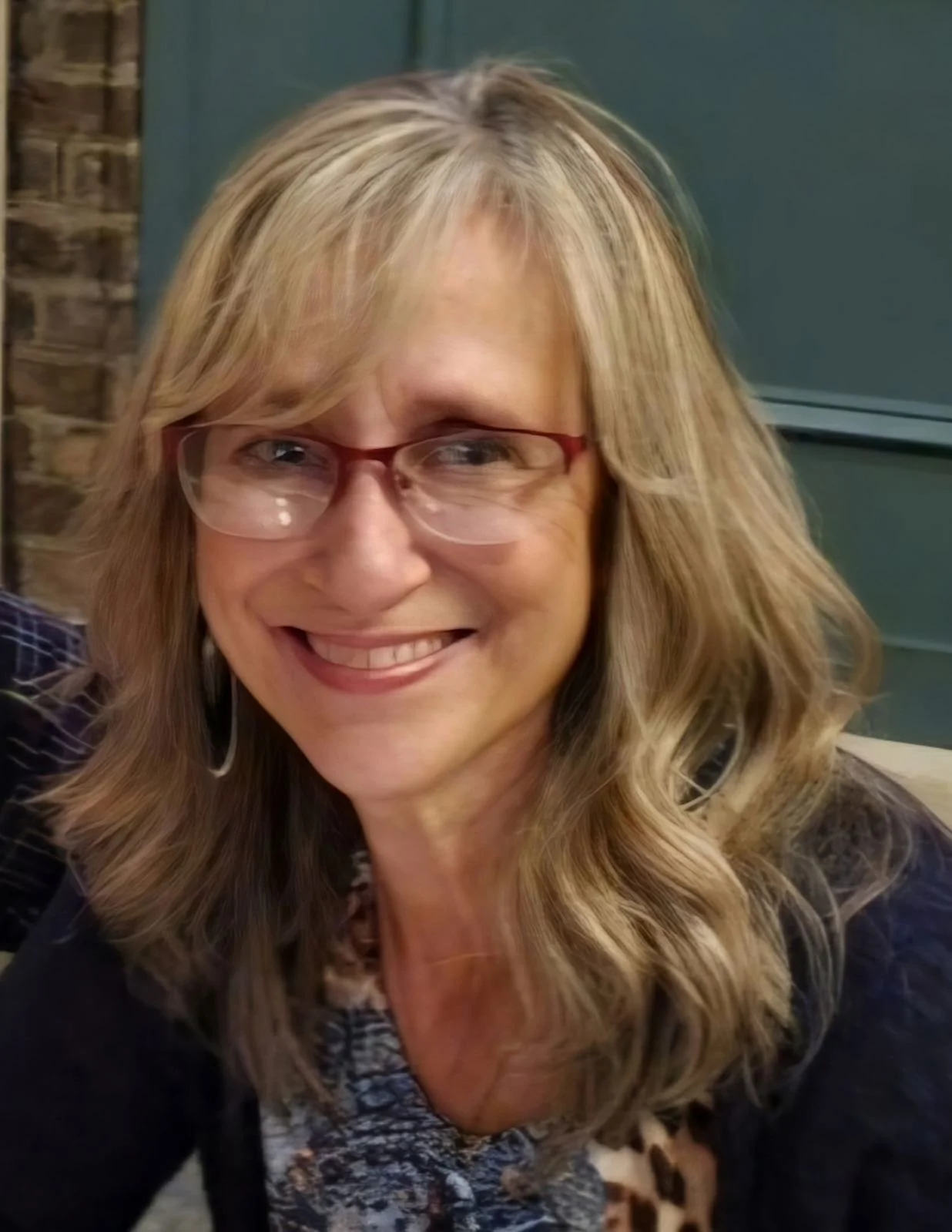 Smiling woman with glasses and long blonde hair indoors.