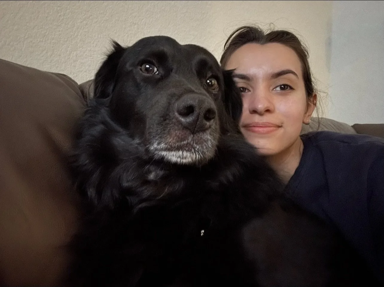 A woman and a black dog lying on a sofa, close together for a selfie.