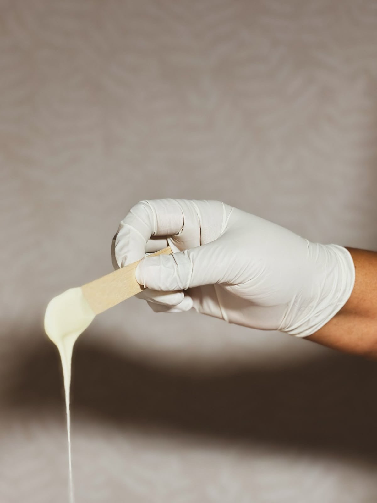 A woman wearing a yellow shirt and black gloves is holding a small plastic cup and a spoon with honey or a similar substance, in an indoor setting.