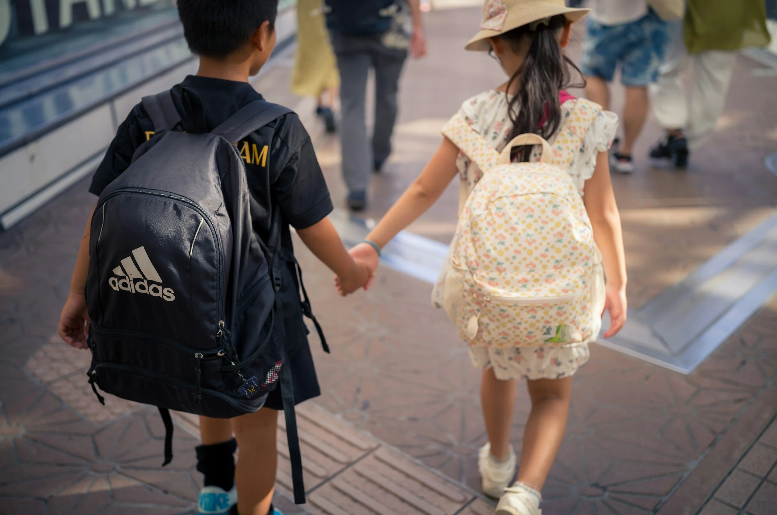 Two elementary-aged children wearing backpacks and holding hands as they walk to school, representing back-to-school anxiety and school transitions.