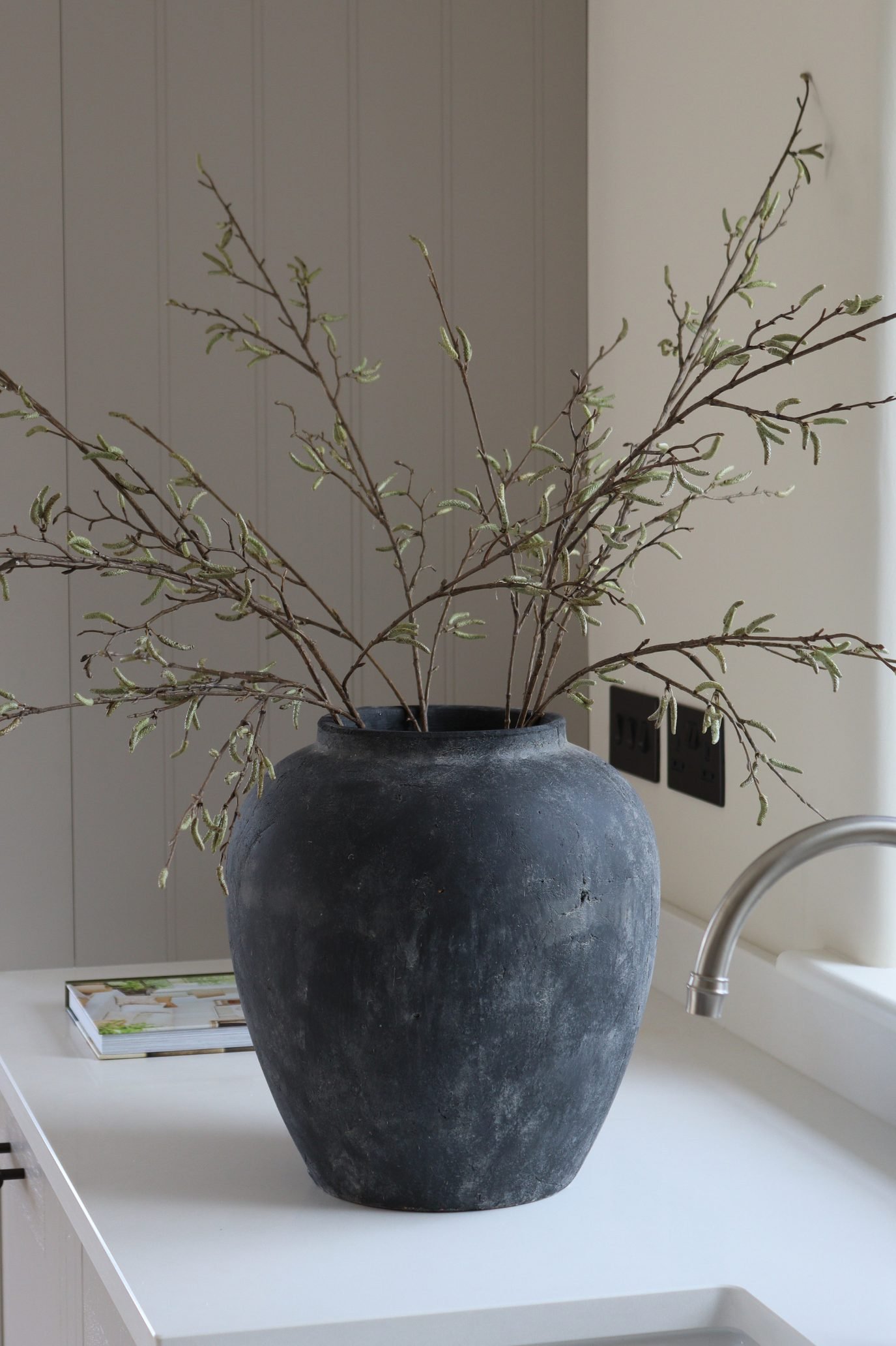Black terracotta modern vase styled with natural branches on a kitchen worktop.