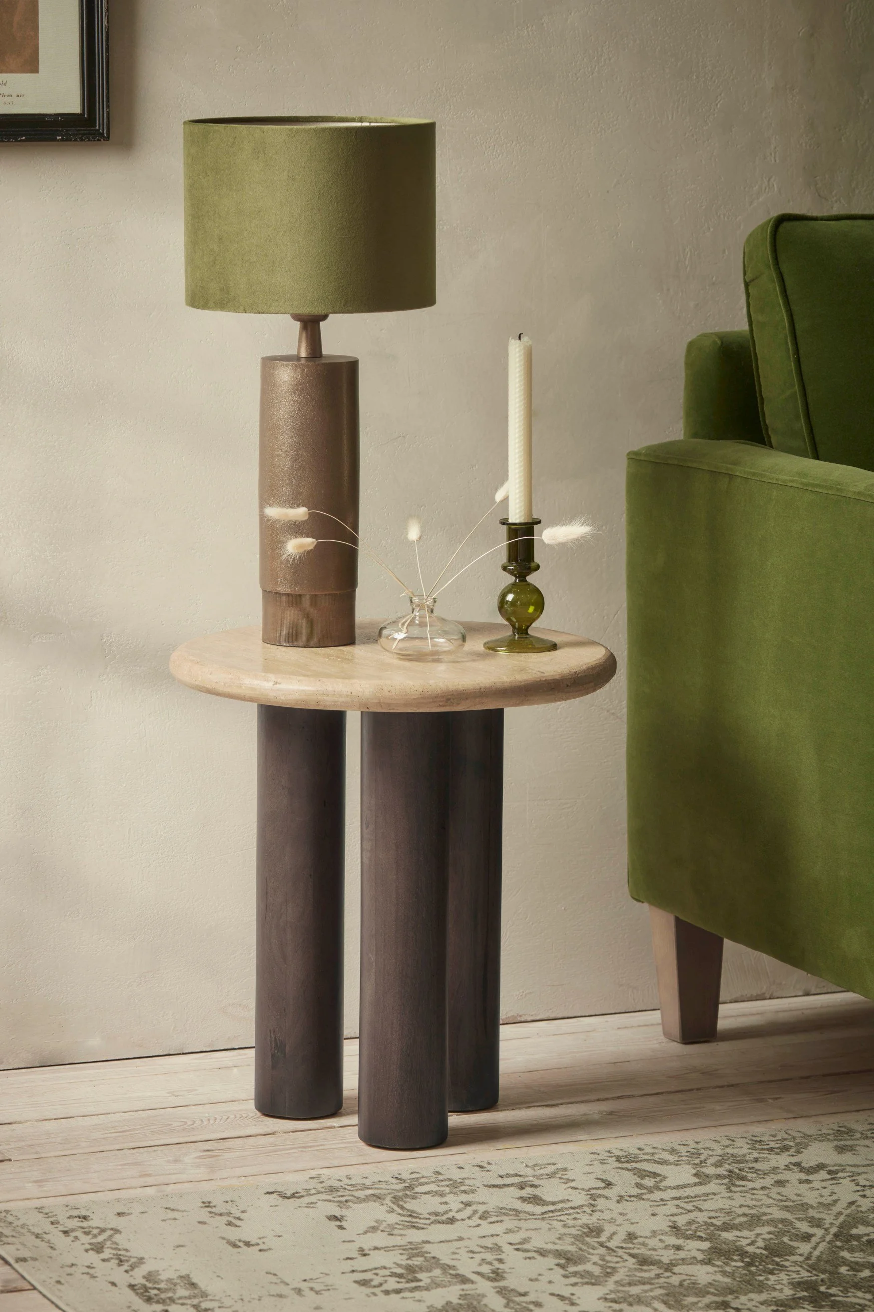 A marble and wood modern console table with a tall stone lamp with a green lamp shade and green candlestick next to a green sofa
