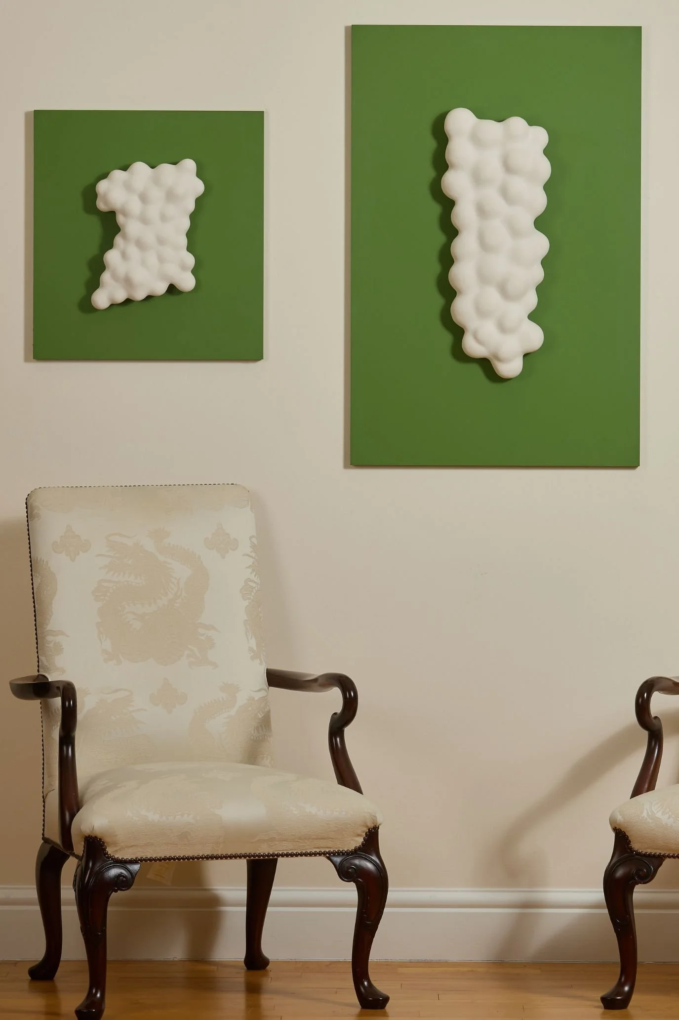 Two white sculptural ceramic wall pieces displayed above an antique chair