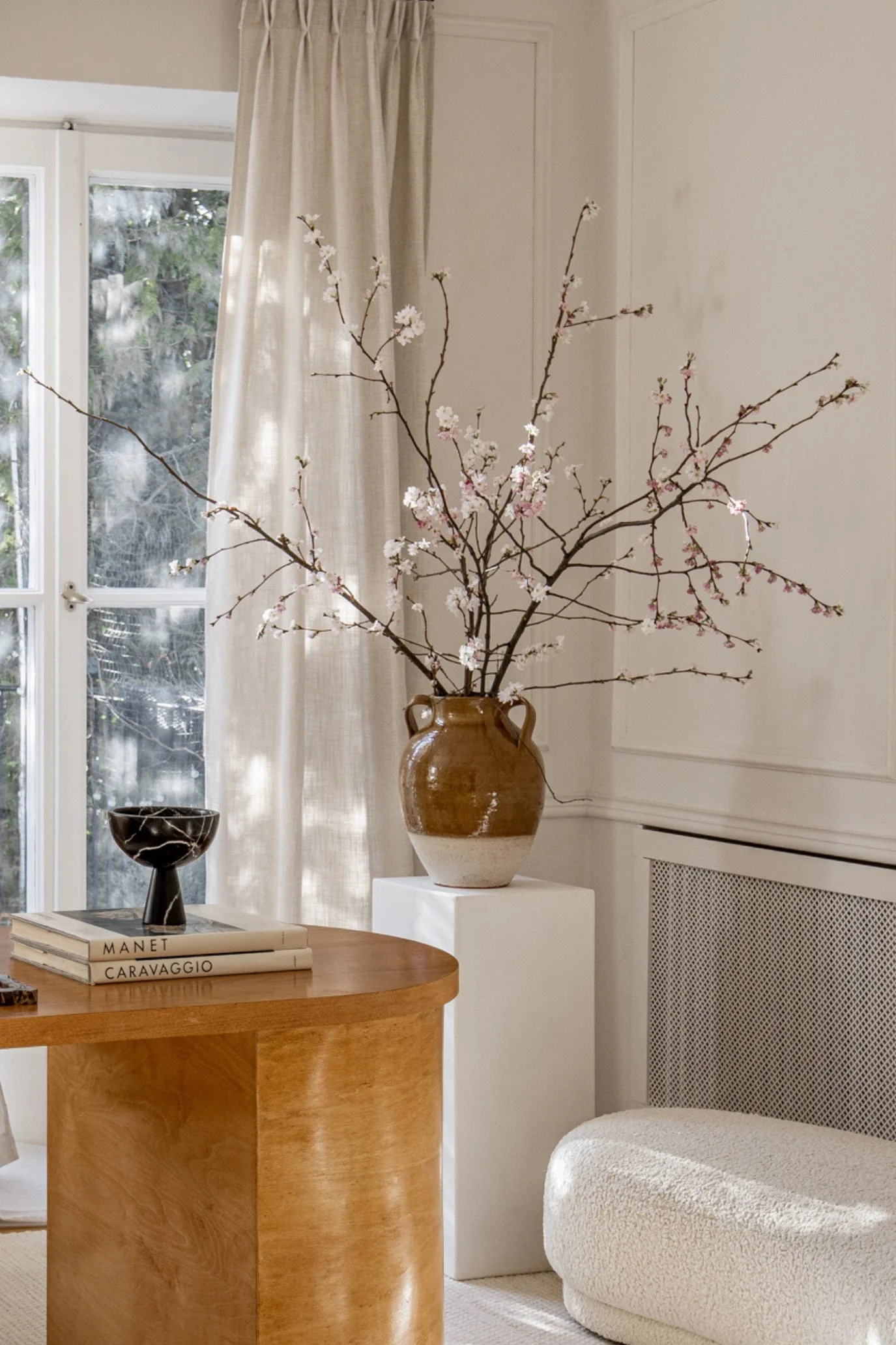 Faux blossom branches arranged in a rustic glazed vase in a neutral living room.