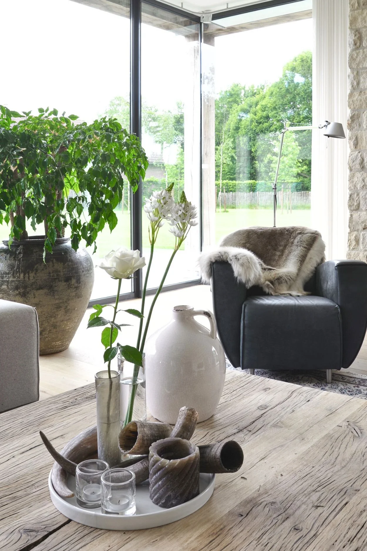 a stylish concrete tray with flowers in vases, two tea light holders a brown candle and three tusks on a rustic wooden table next to a white stone vessel.