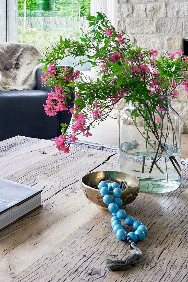 A wooden table with a large vintage vase filled with branches of pink Azaleas