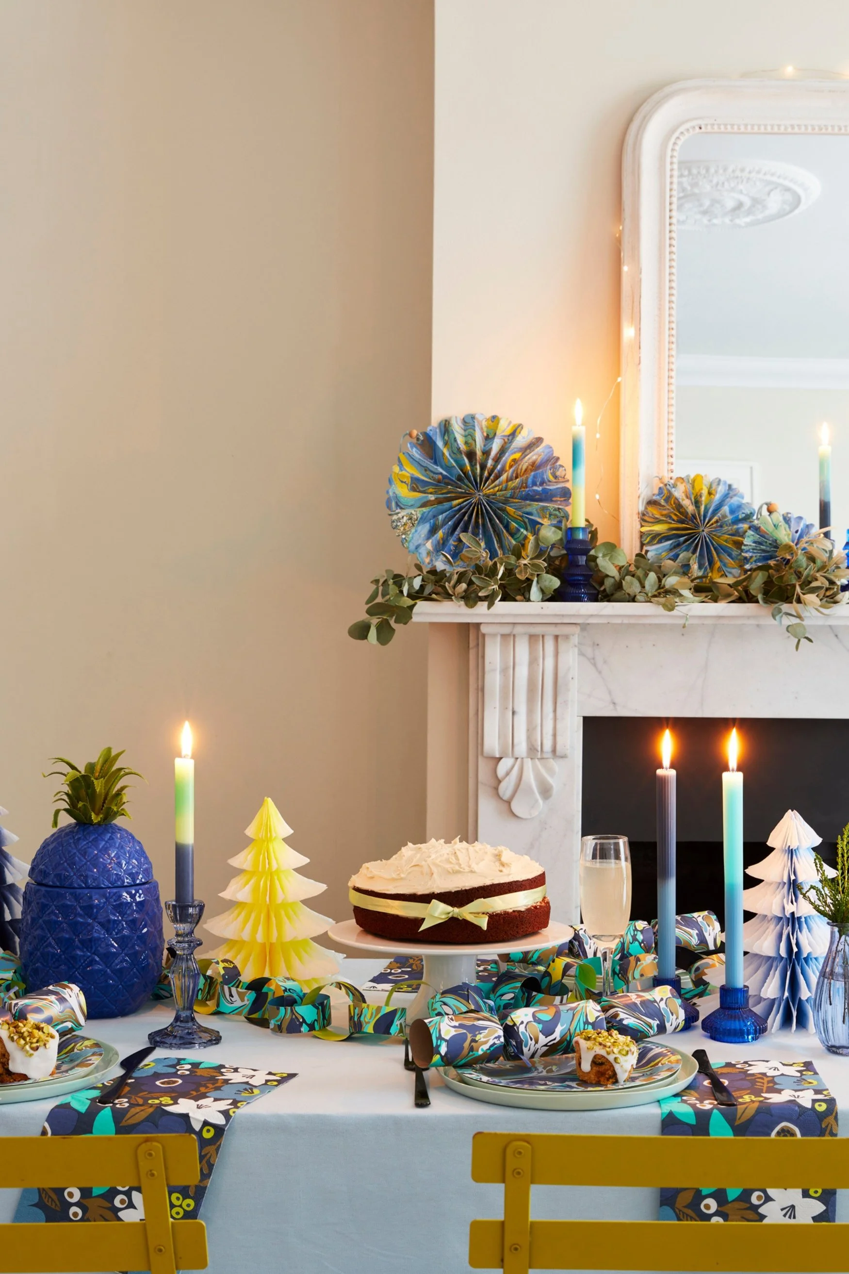 A table set with a cake yellow christmas tree and marbled candles in blues and aqua