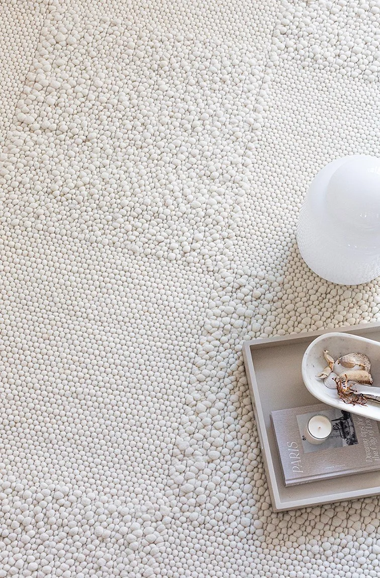 A white wall checkered rug with a tray with a book, tea light and dish on it