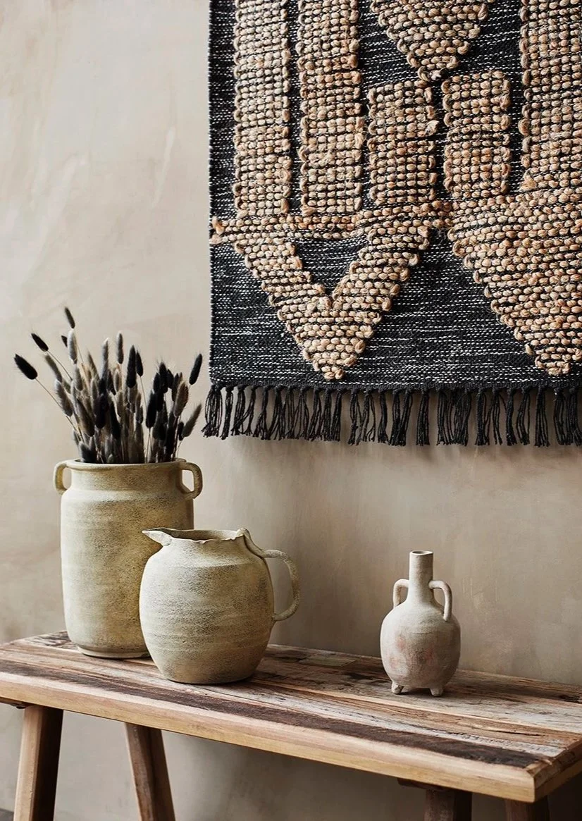 Dried buny taił grasses in natural stone pot next to a woven wall hanging