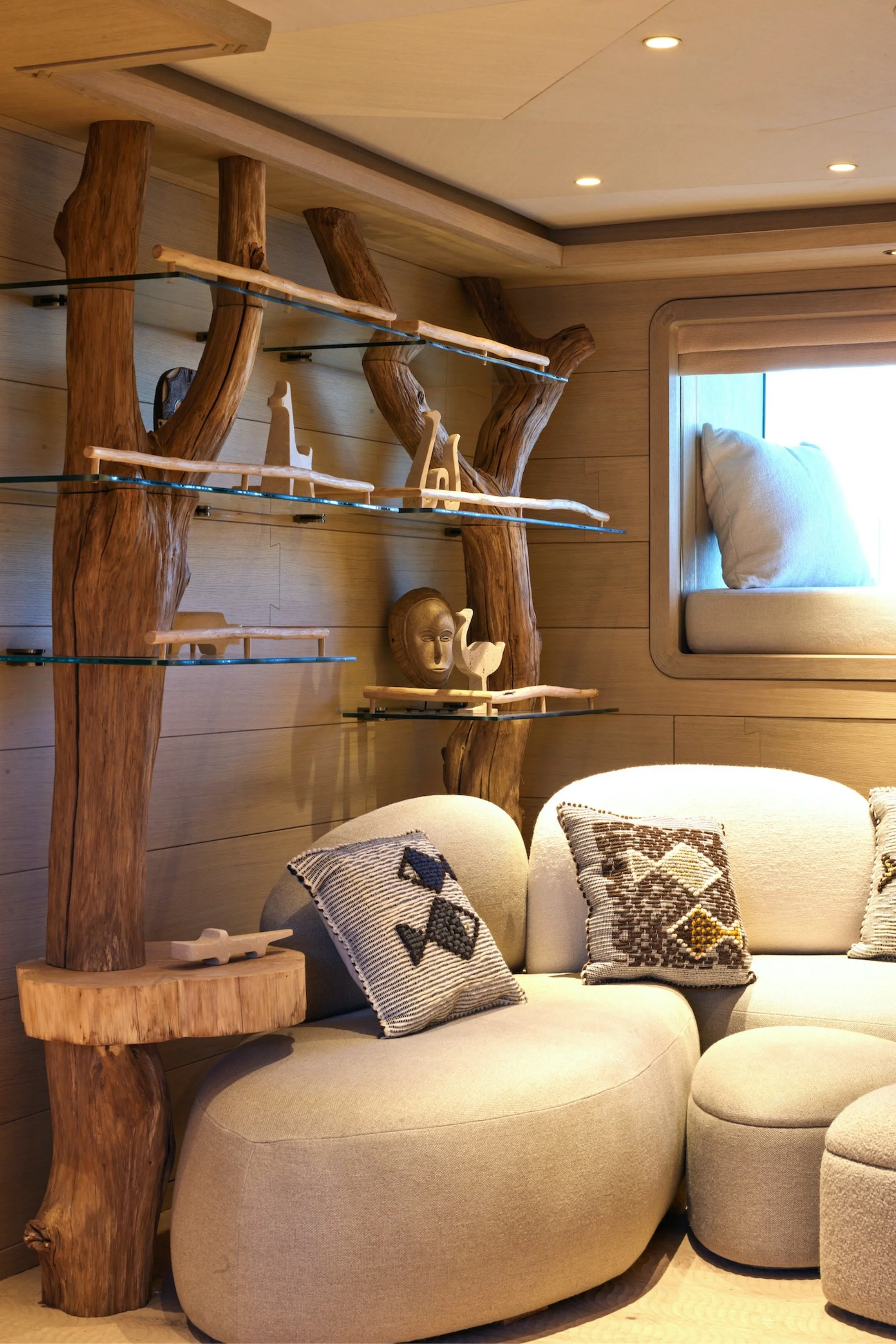 A shelving unit made from two trees with glass shelves and wooden animals displayed on the shelves