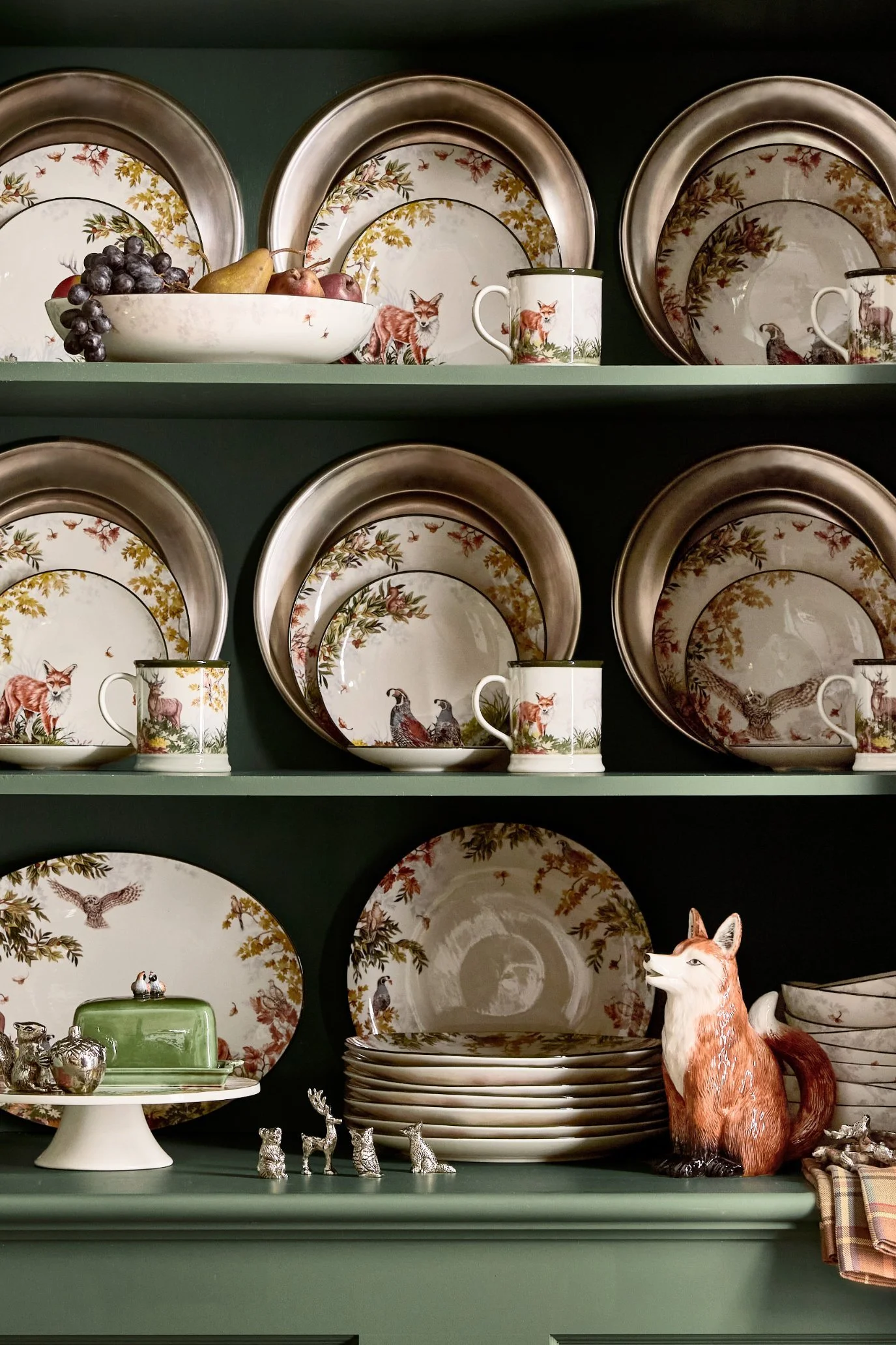 Hand-painted stoneware plates with woodland animal designs displayed inside a traditional kitchen dresser.