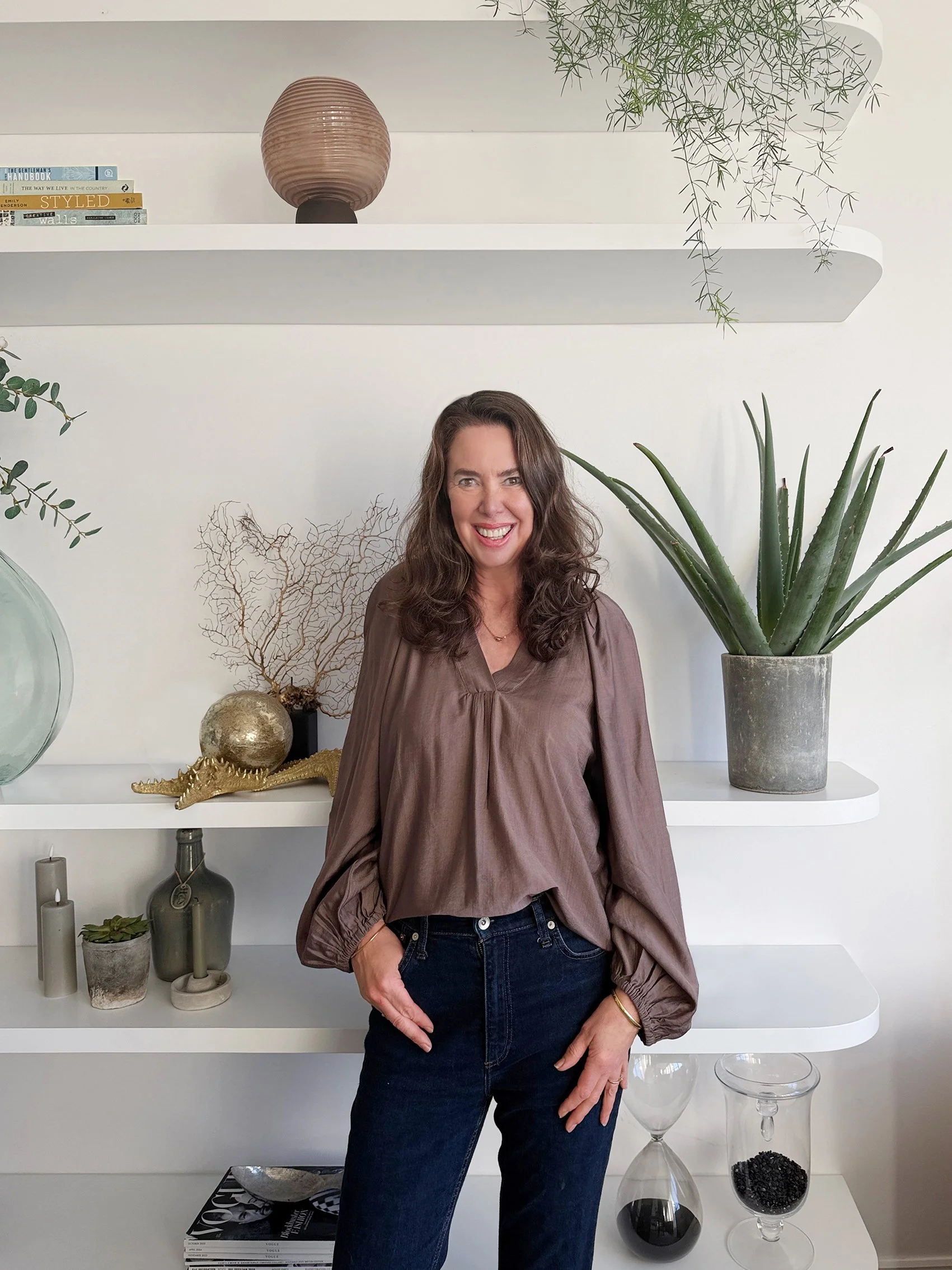 Image of Sandra van Aalst wearing a brown top and jeans in front of shelving