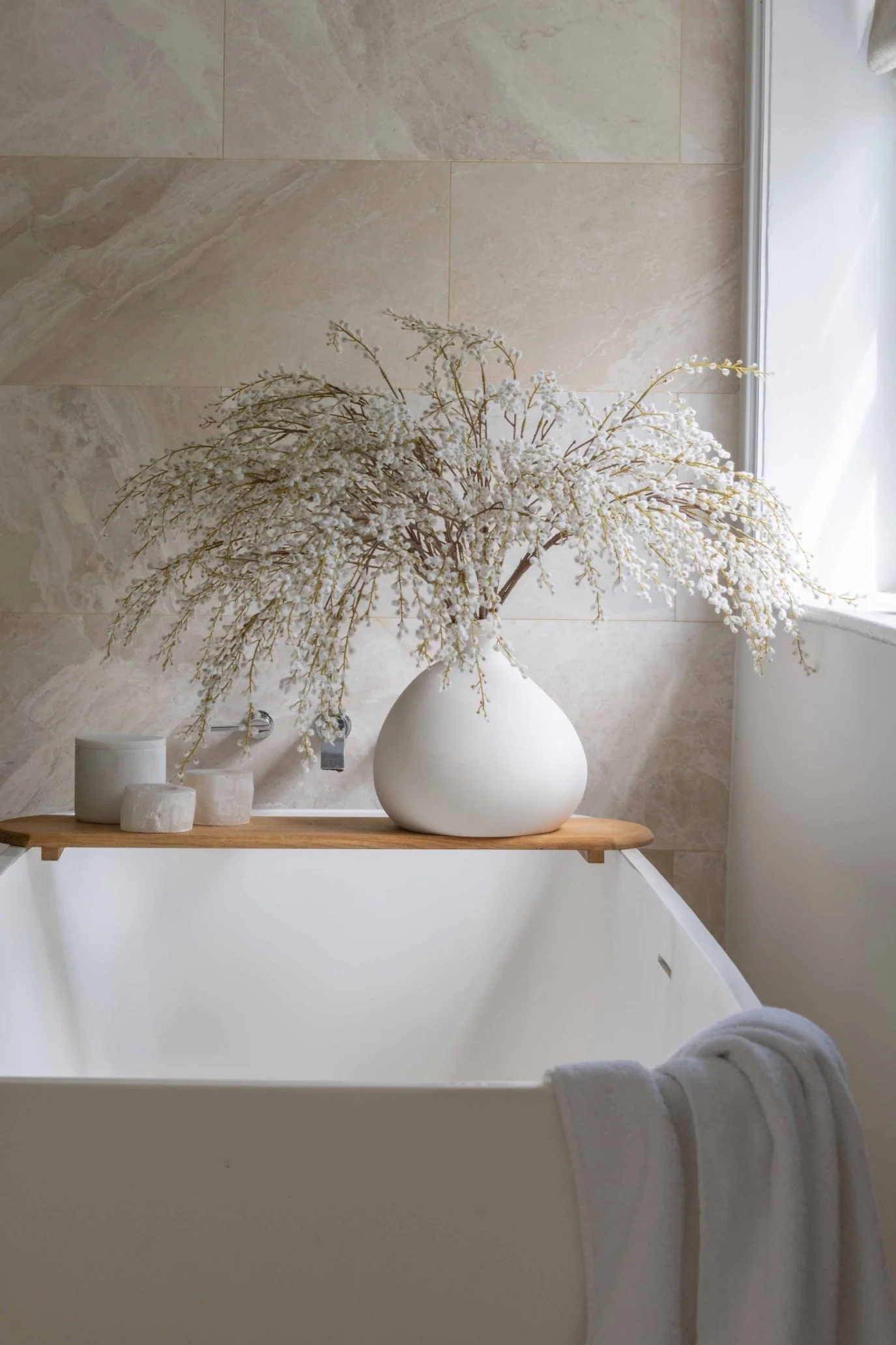 White faux flowering branches arranged in a rounded white vase in a neutral bathroom.
