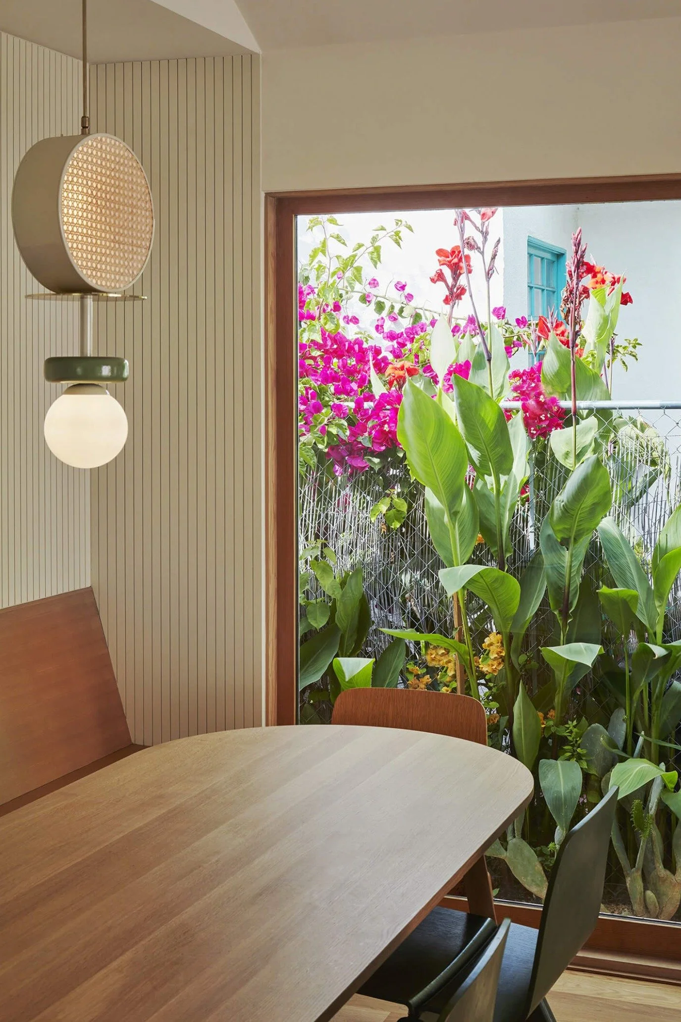 Contemporary dining area with fluted walls, built-in banquette seating, tropical plants and sculptural pendant lighting.