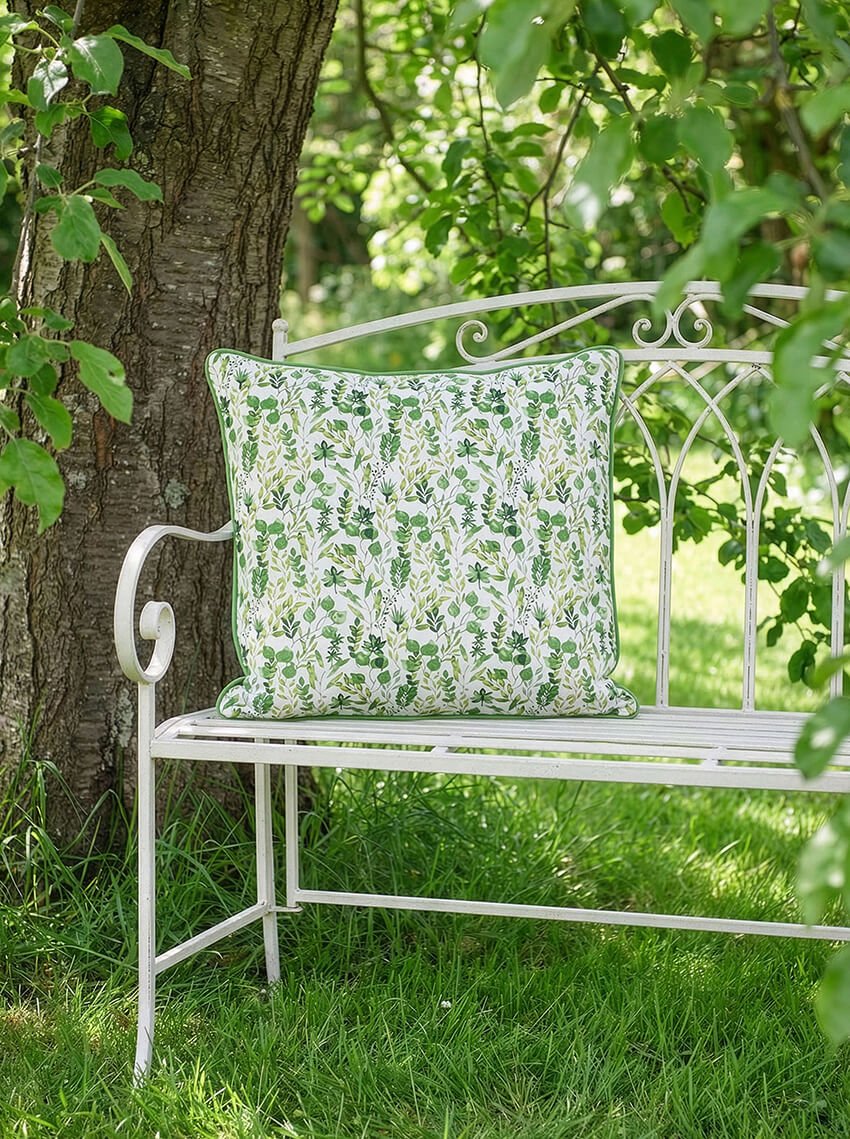 White wrought iron bench with a green leaf-print outdoor cushion in a garden