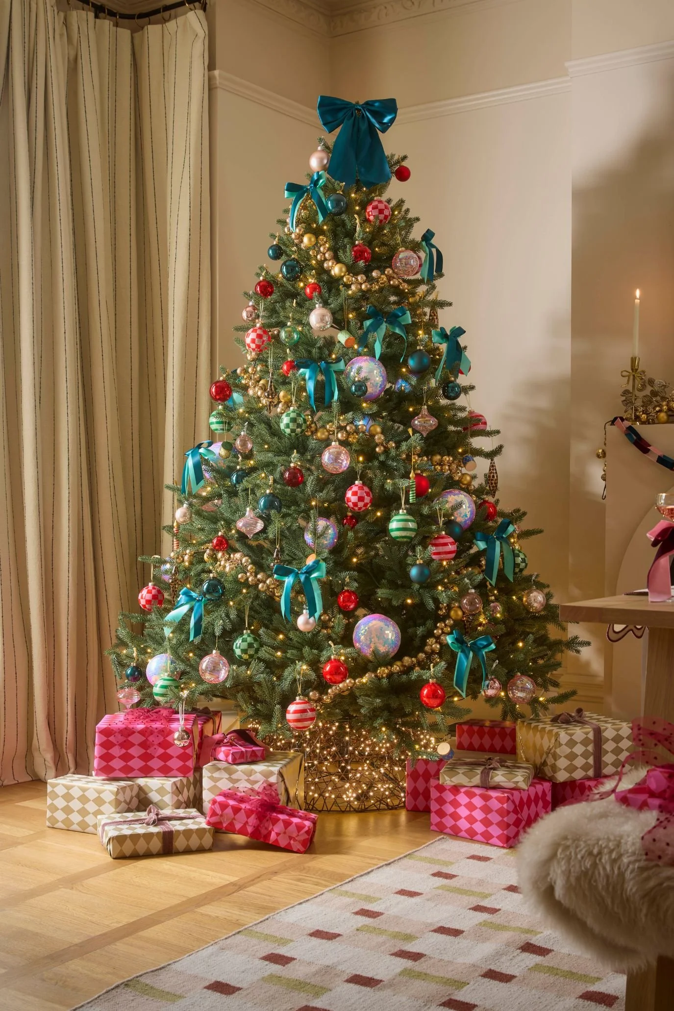 Christmas tree decorated with aqua ribbon bows, colourful baubles and warm lights, surrounded by pink and patterned presents.
