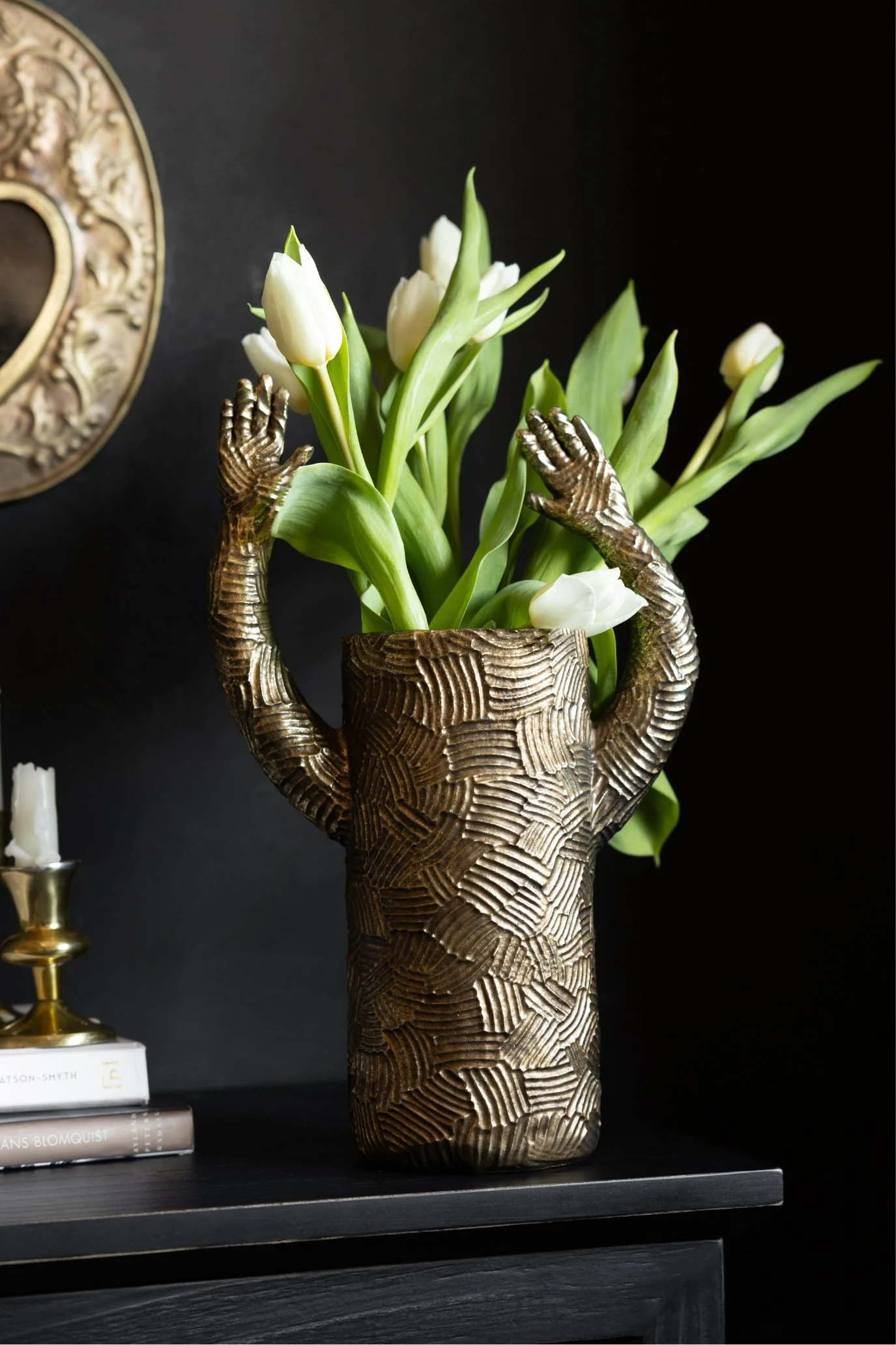 Textured gold vase with sculpted waving arms filled with tulips.